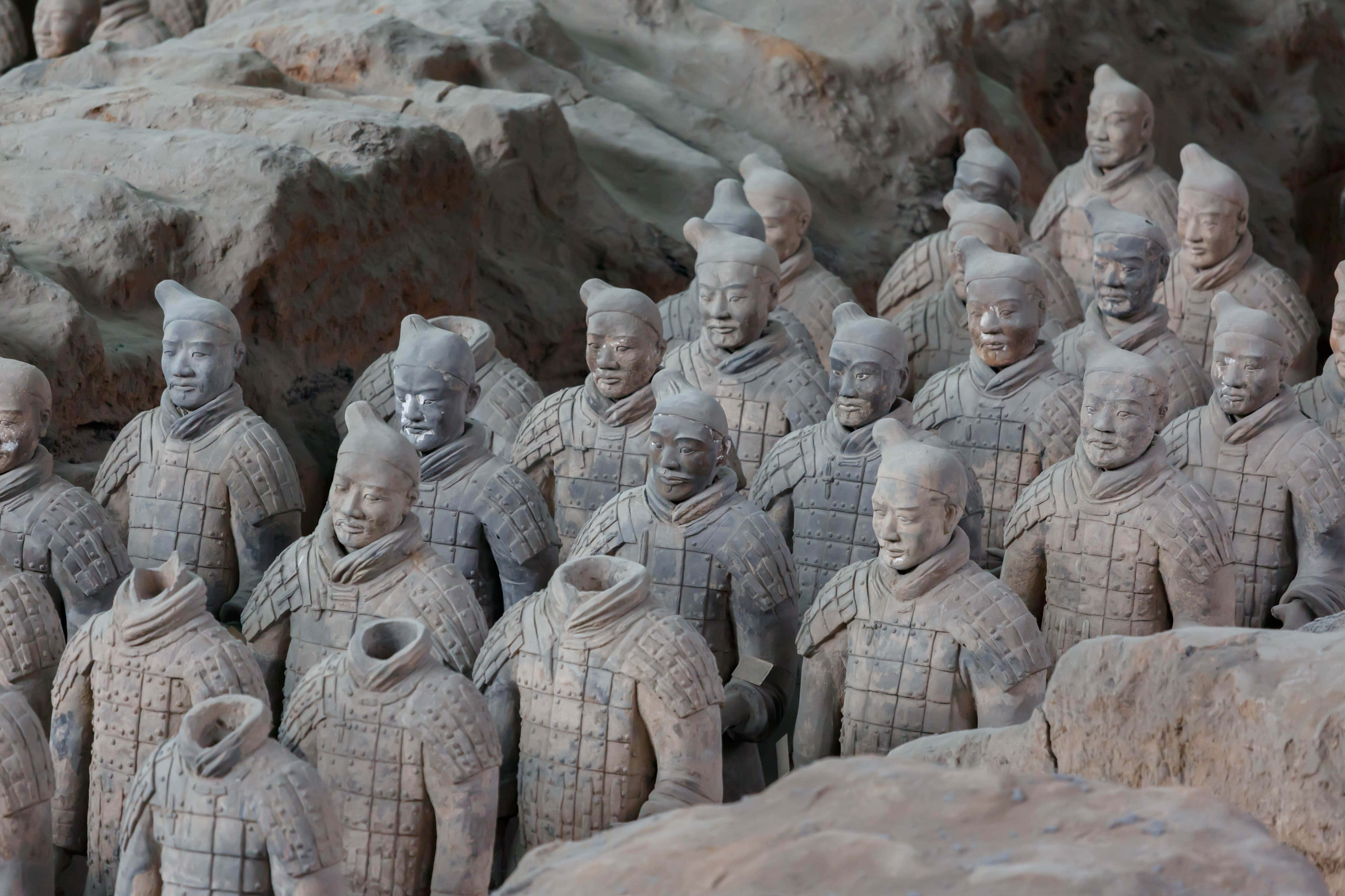 中國陶俑墓葬藝術 壁紙 — 一排排古老的兵馬俑以大地色調站立在發掘坑內，每個都有獨特的面部表情和詳細的盔甲。