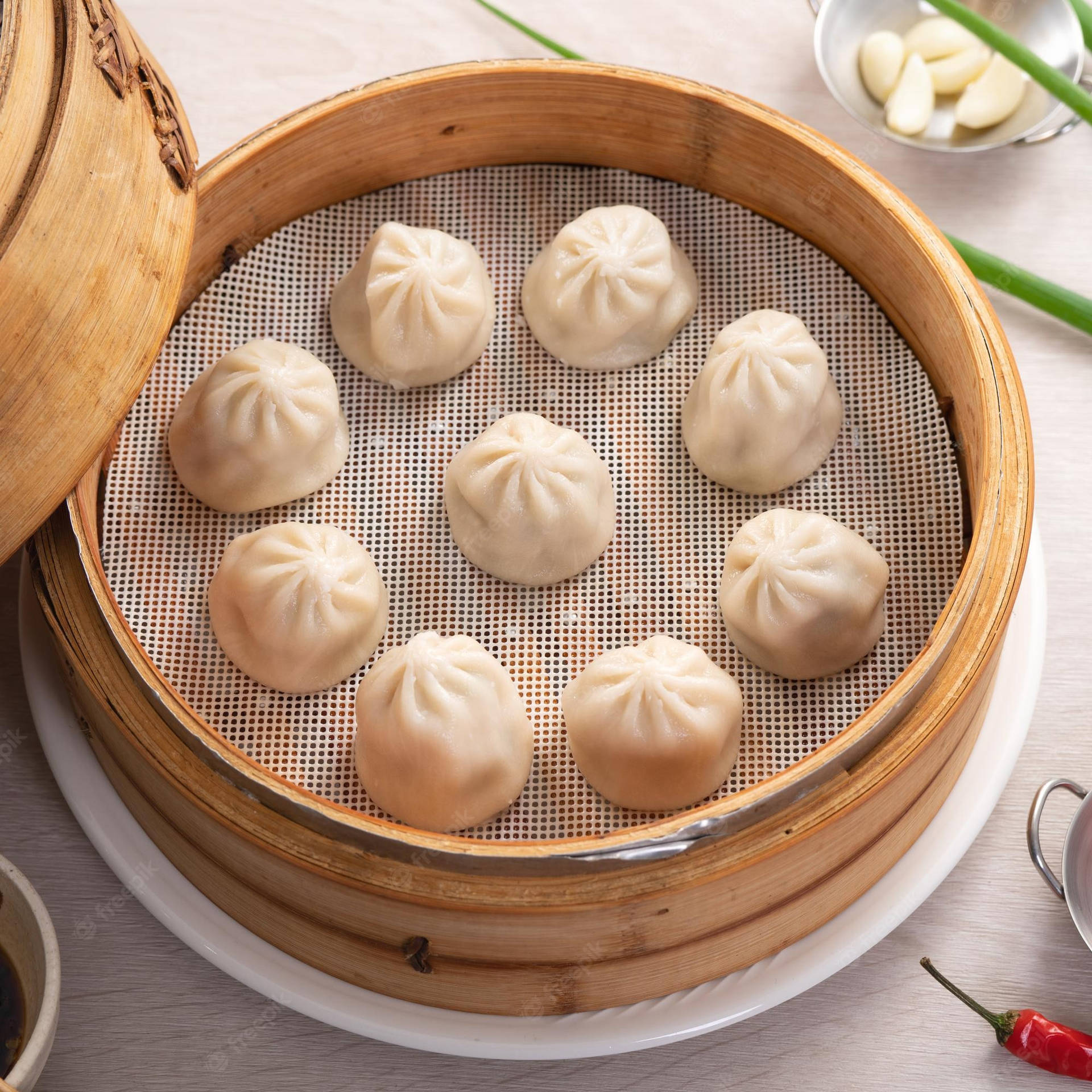 竹蒸籠裡新鮮嘅餃子配蒜頭、蔥花同辣椒。