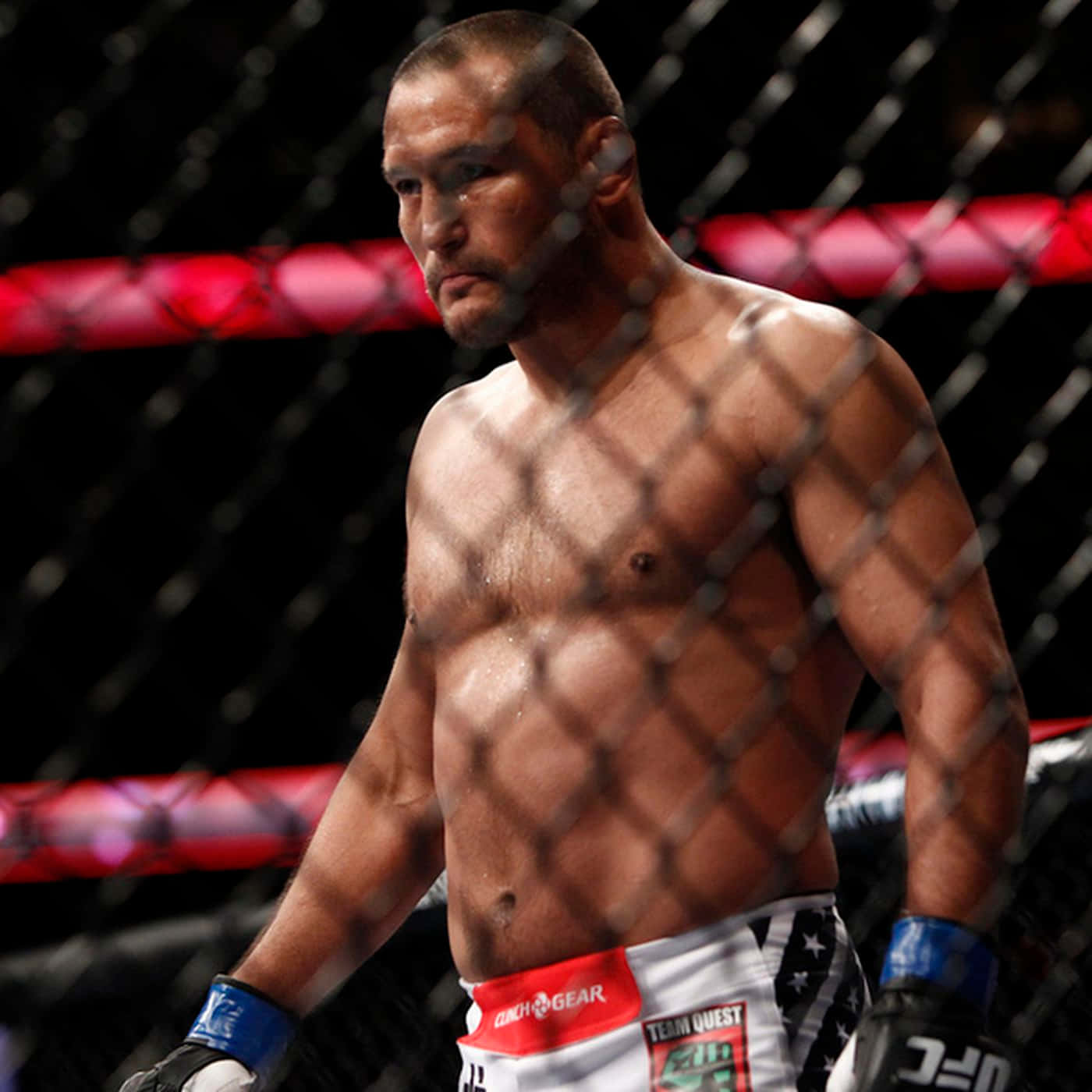 一位赤裸上身的MMA戰士在籠內戴著手套和短褲。