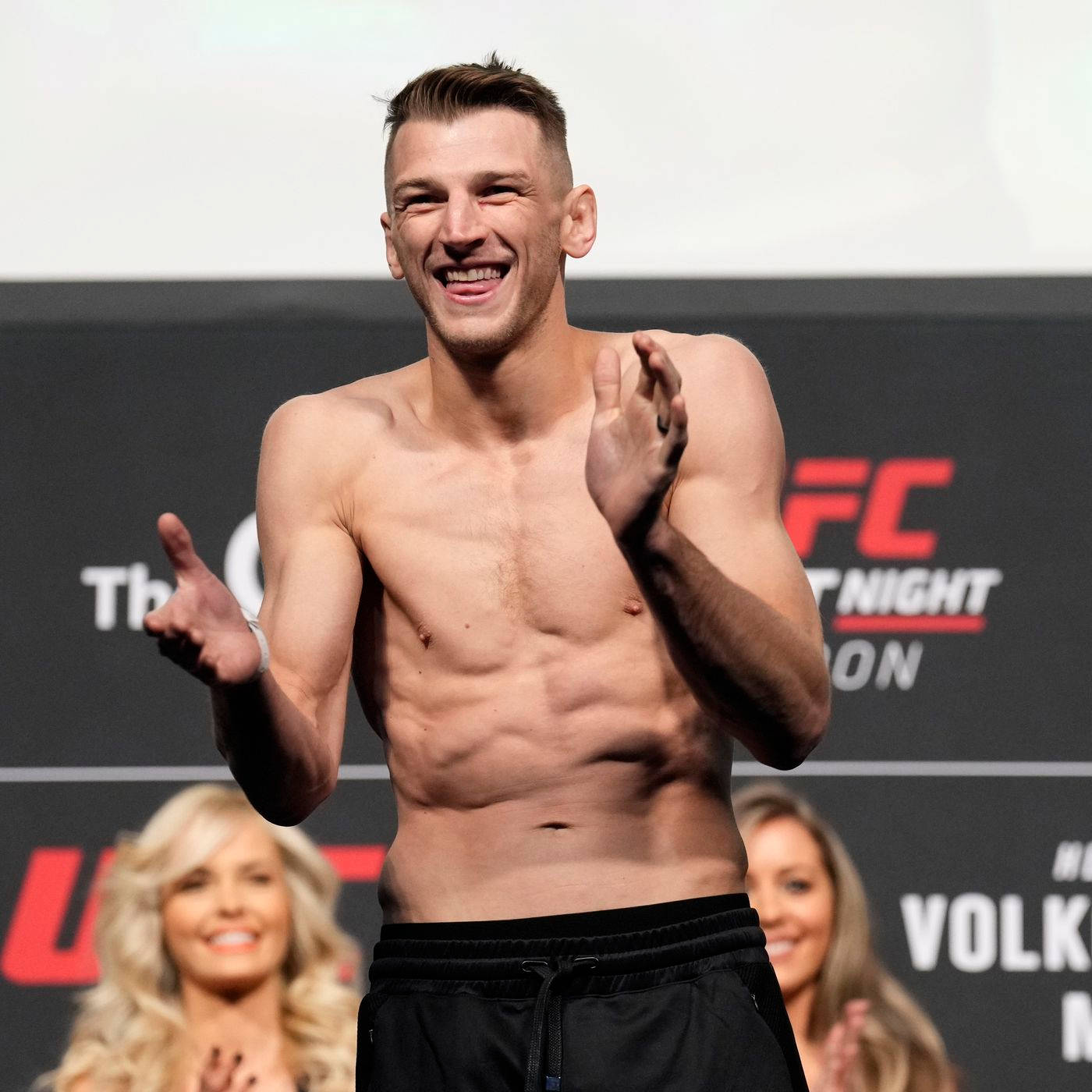UFC拳手在過磅活動中微笑鼓掌，身後有粉絲。