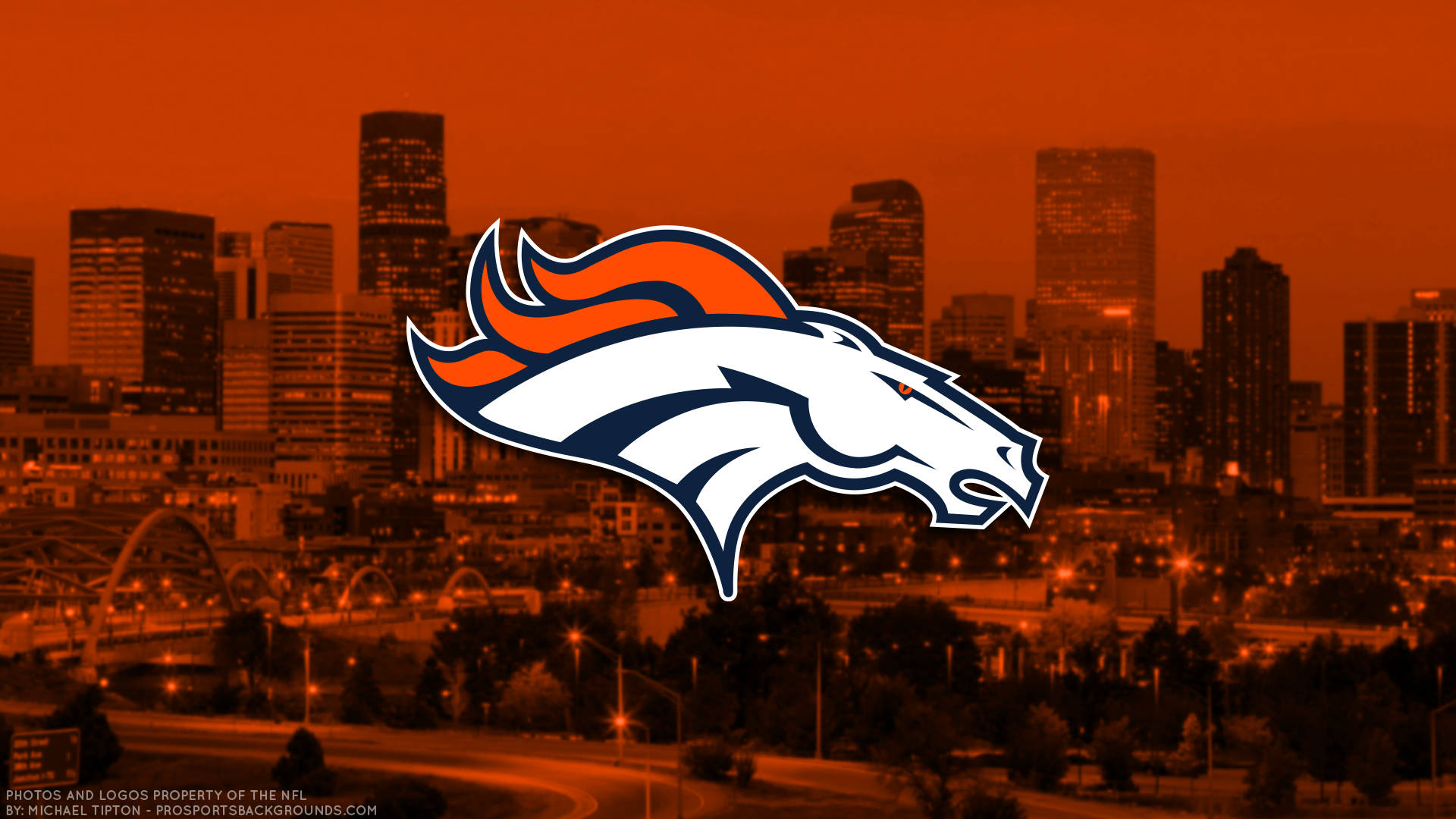 Denver Broncos City Background 壁紙 — 丹佛野馬隊標誌漂浮在沐浴在熾熱橙色夕陽餘暉中的城市天際線上。