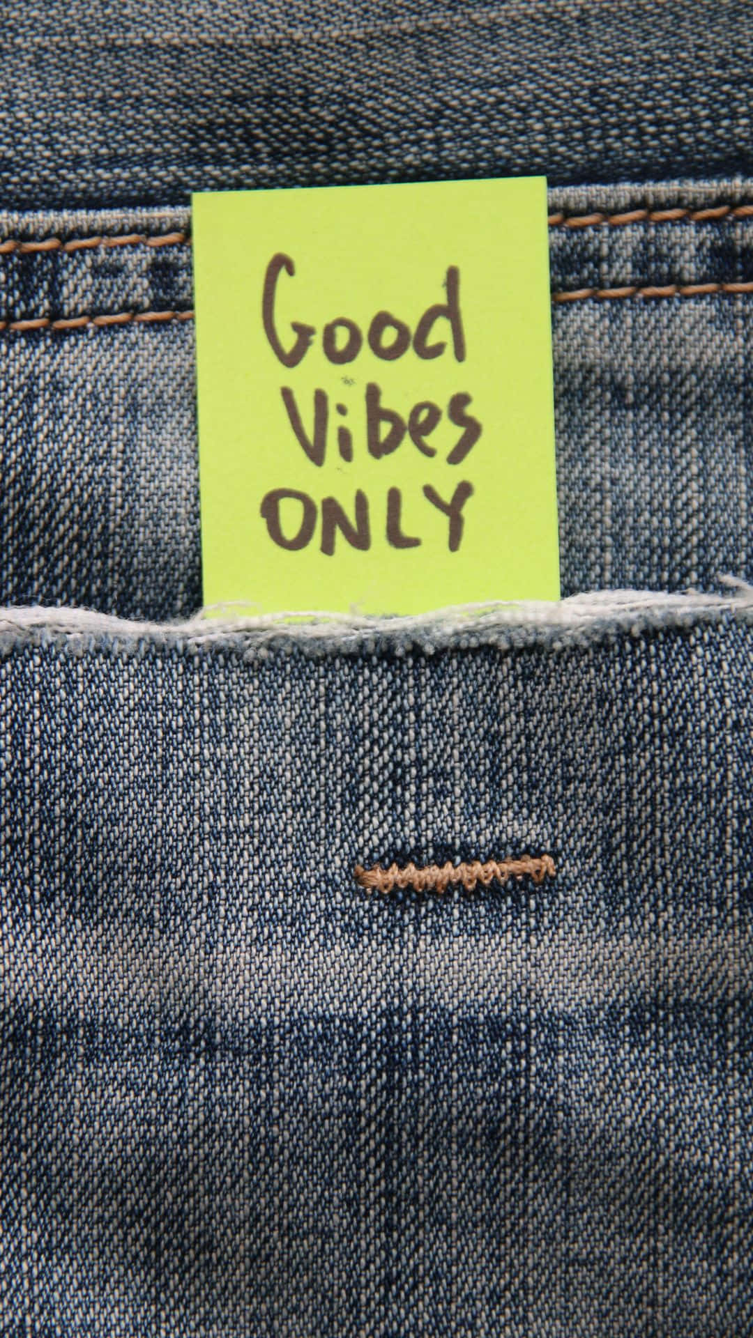 一張黃色便利貼，上面寫著 Good Vibes ONLY，放在牛仔褲口袋裡。