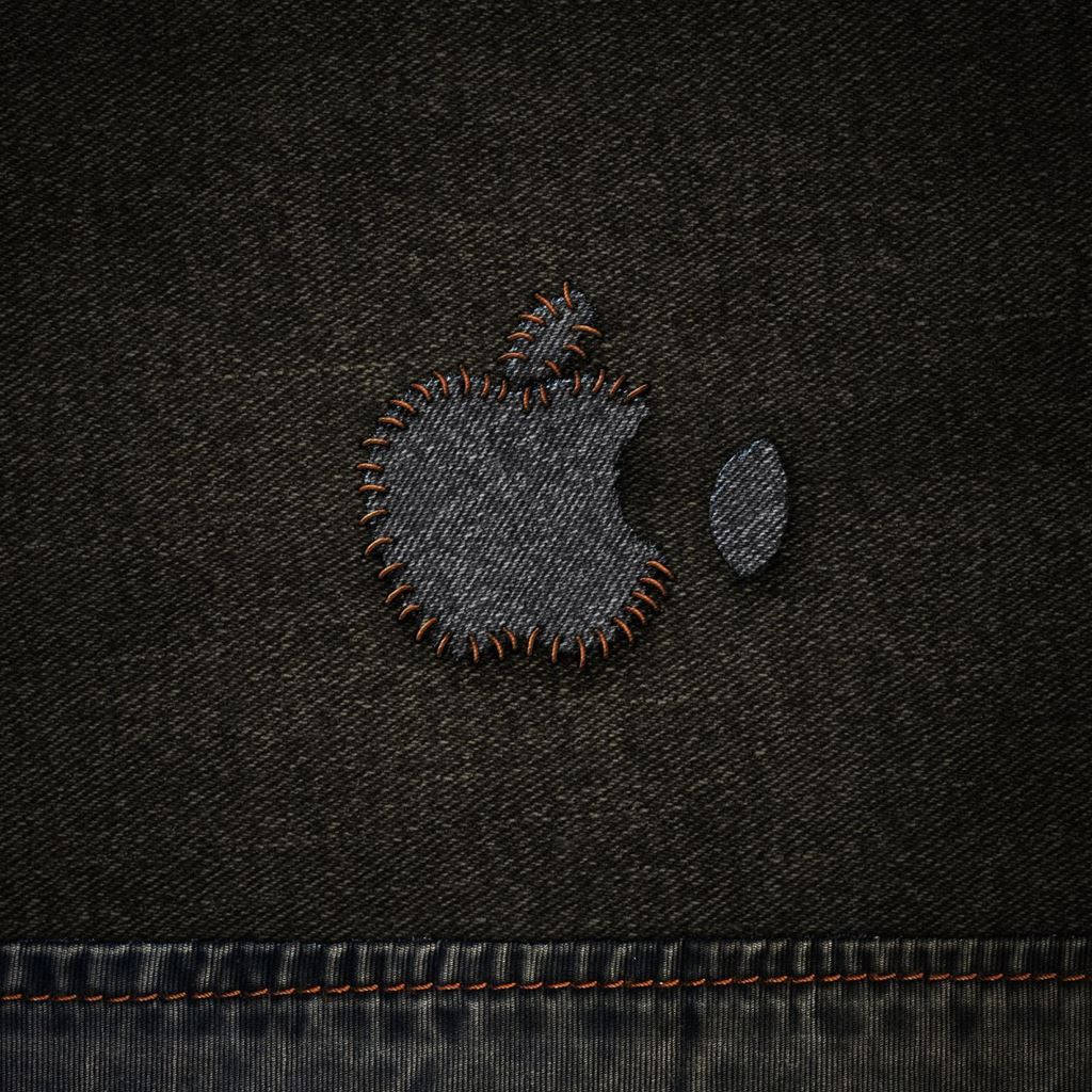 丹寧黑布料配 Apple 標誌設計 壁紙 — 近距離拍攝的Apple標誌，以橙色線縫在深色牛仔布上，背景為有紋理的布料。