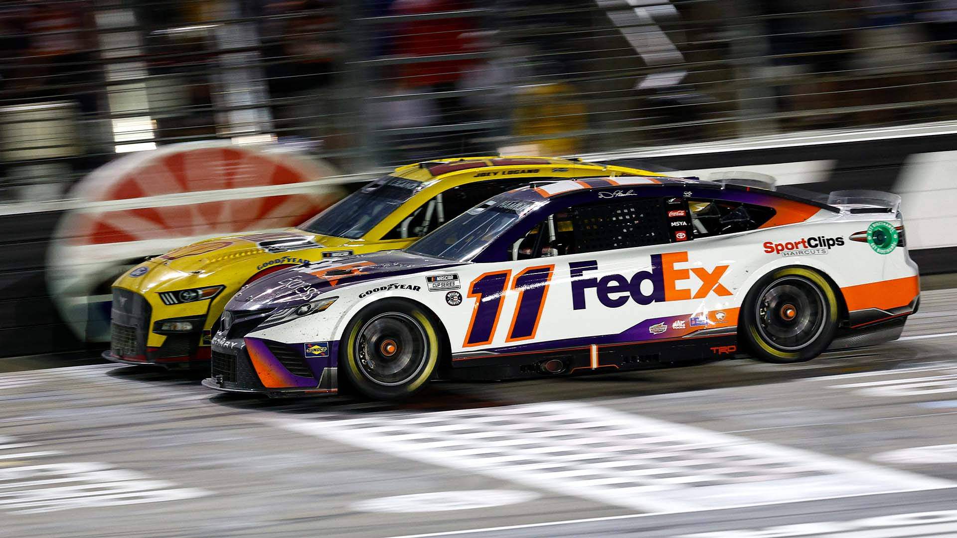 兩輛NASCAR賽車在夜間以動態模糊競速。