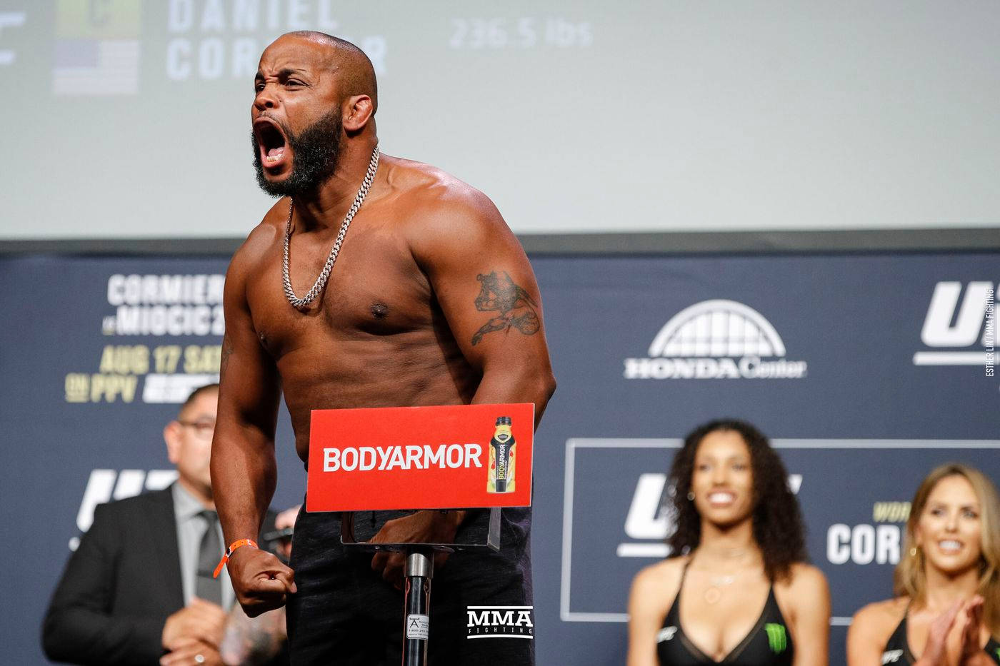 丹尼爾·科爾米爾 UFC 210 壁紙 — 一位肌肉發達的戰士在UFC稱重活動中高舉BodyArmor標誌牌，發出勝利的咆哮。