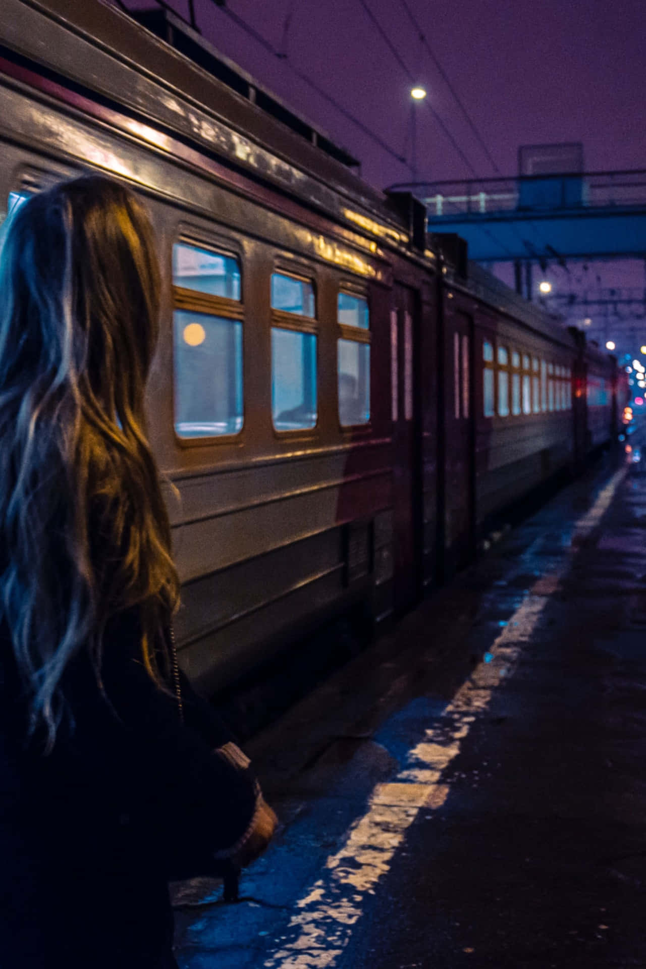 女子在紫色天空下夜晚雨中的火車站等候。