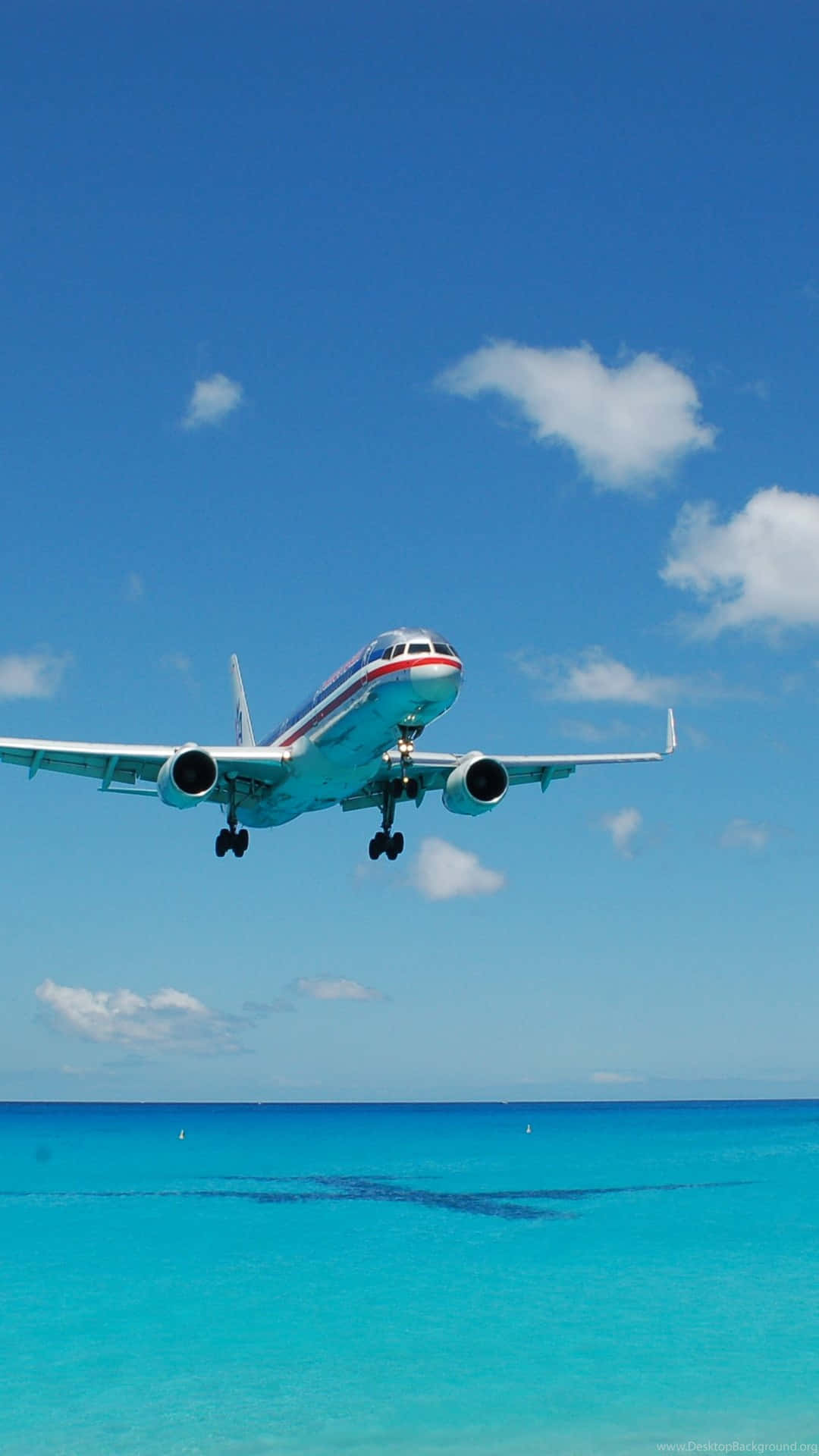 乘私人飛機翱翔天際 壁紙 — 一架商用飛機在晴朗藍天和零星白雲下，向著碧綠色的海洋下降。