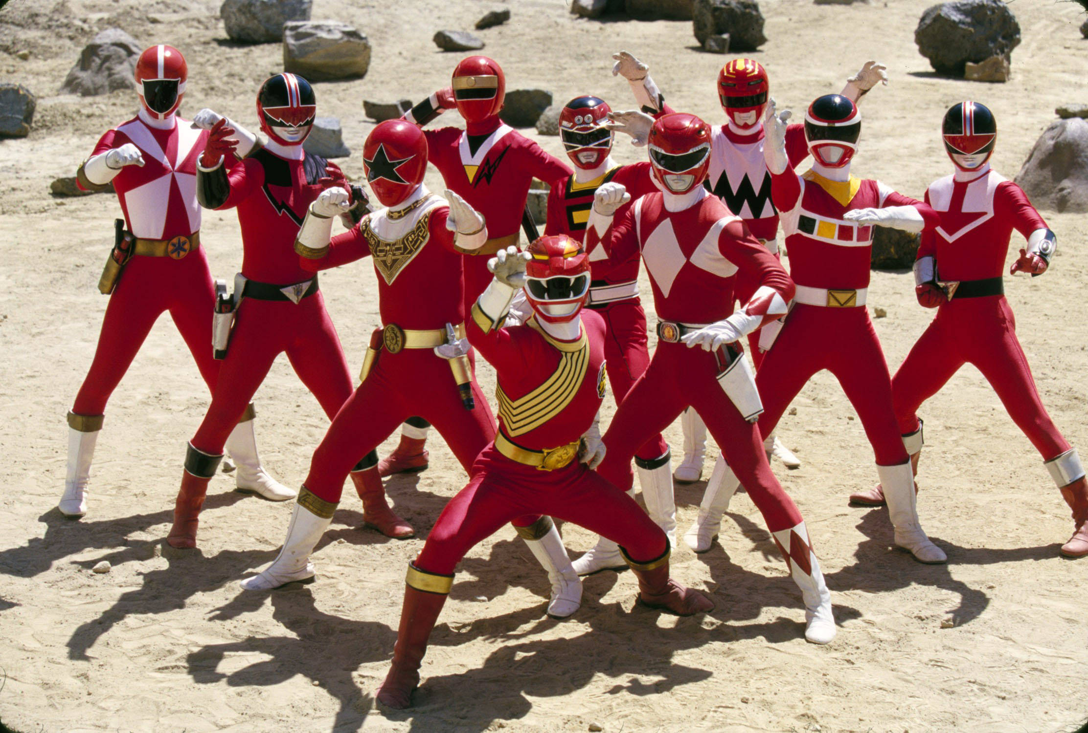 Power Rangers Forever Red 壁紙 — 九位紅白裝甲英雄在陽光明媚的岩石沙漠景觀中擺出動感姿勢。