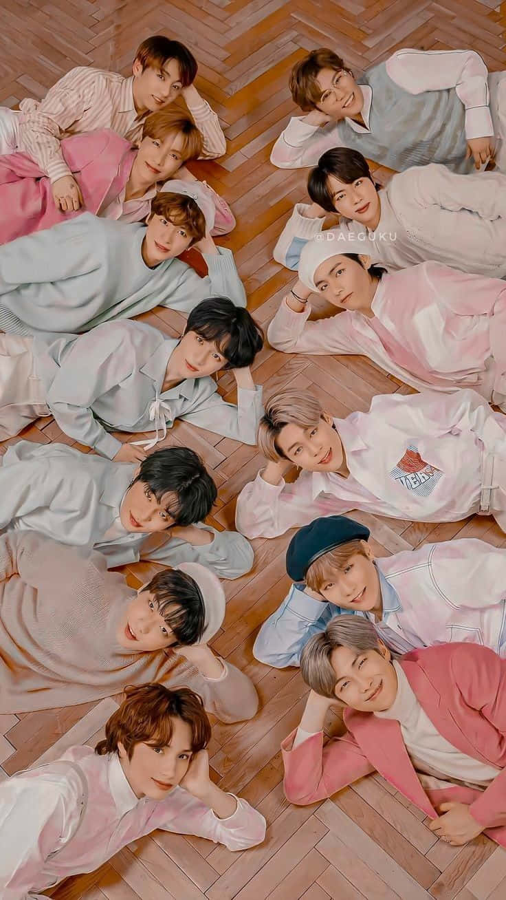 Big Hit Entertainment 桌布 壁紙 — 九位身穿柔和色調服裝的年輕男性躺在木地板上圍成一個圓圈，對著鏡頭微笑。