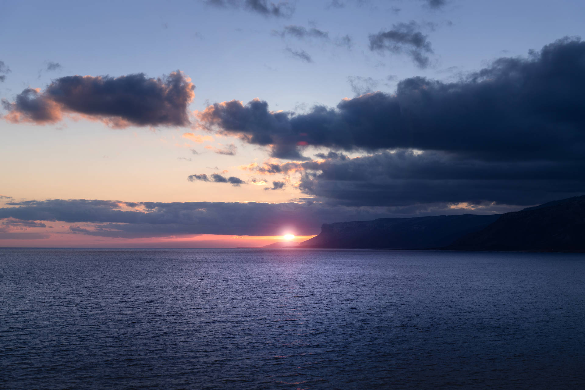 平靜海面上的日落，有烏雲和遠方懸崖