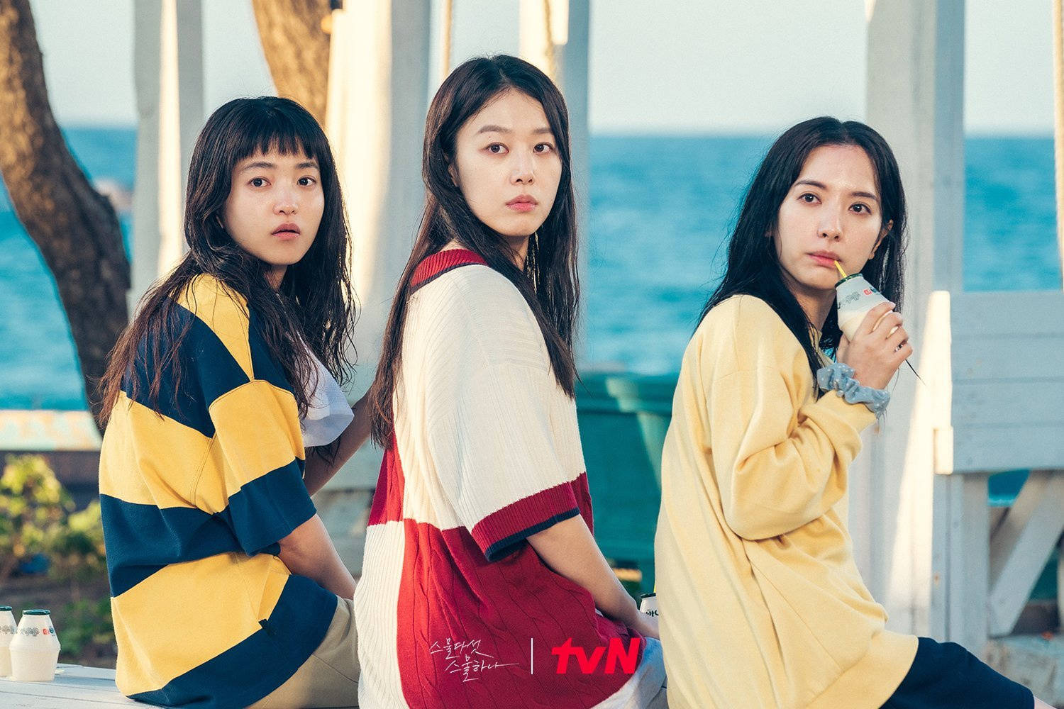 三位年輕女性穿著色彩繽紛的衣服，在日落時分坐在海邊。