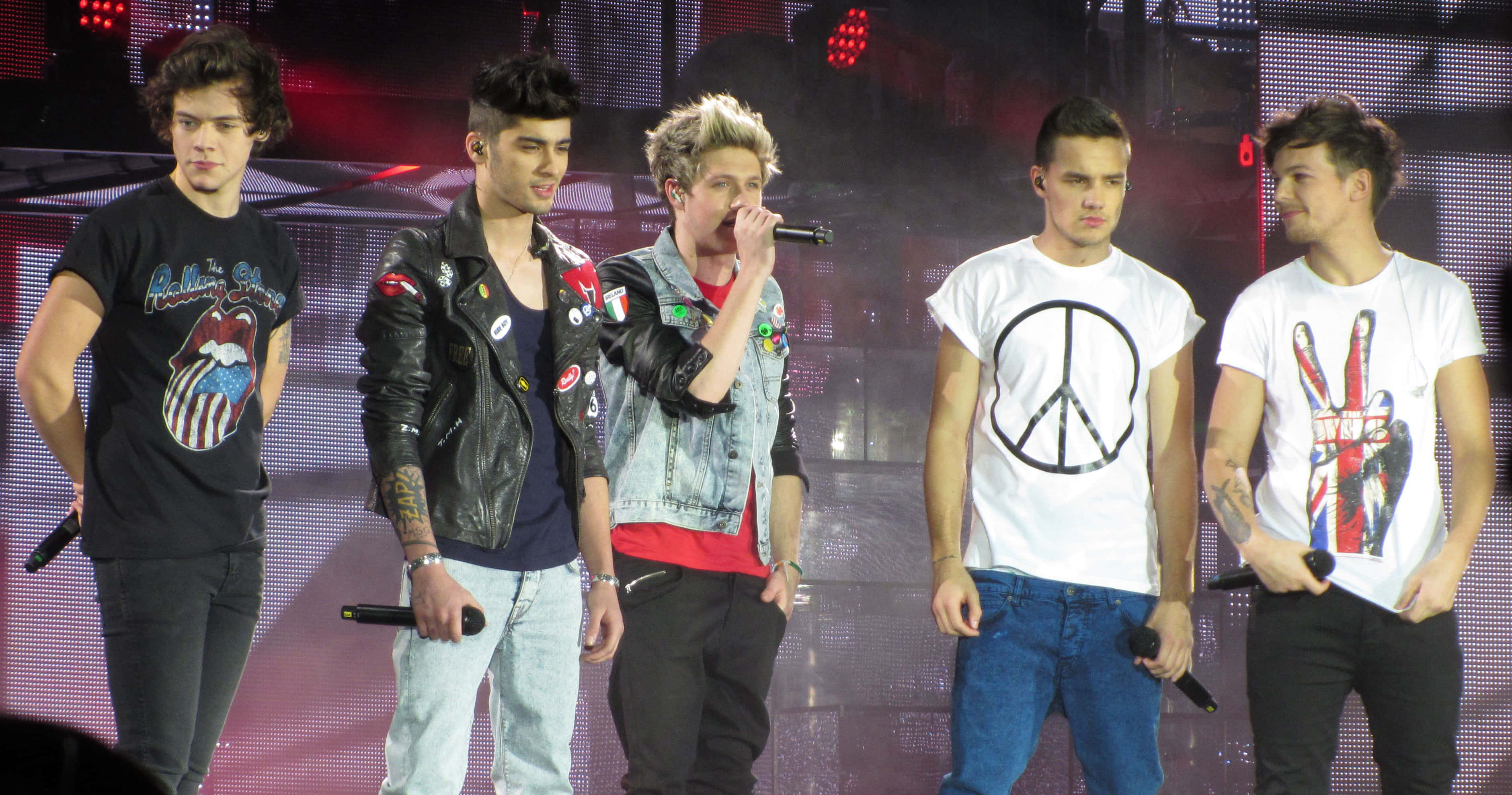 One Direction 桌布 壁紙 — 五位年輕男音樂家在燈光璀璨的舞台上表演，身後有LED屏幕和煙霧效果。