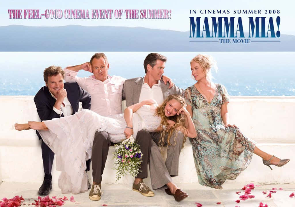 Mamma Mia 桌布 壁紙 — 五位微笑的演員在白色石台上擺姿勢，俯瞰著晴朗天空下明亮的藍色大海和遠處的山脈。