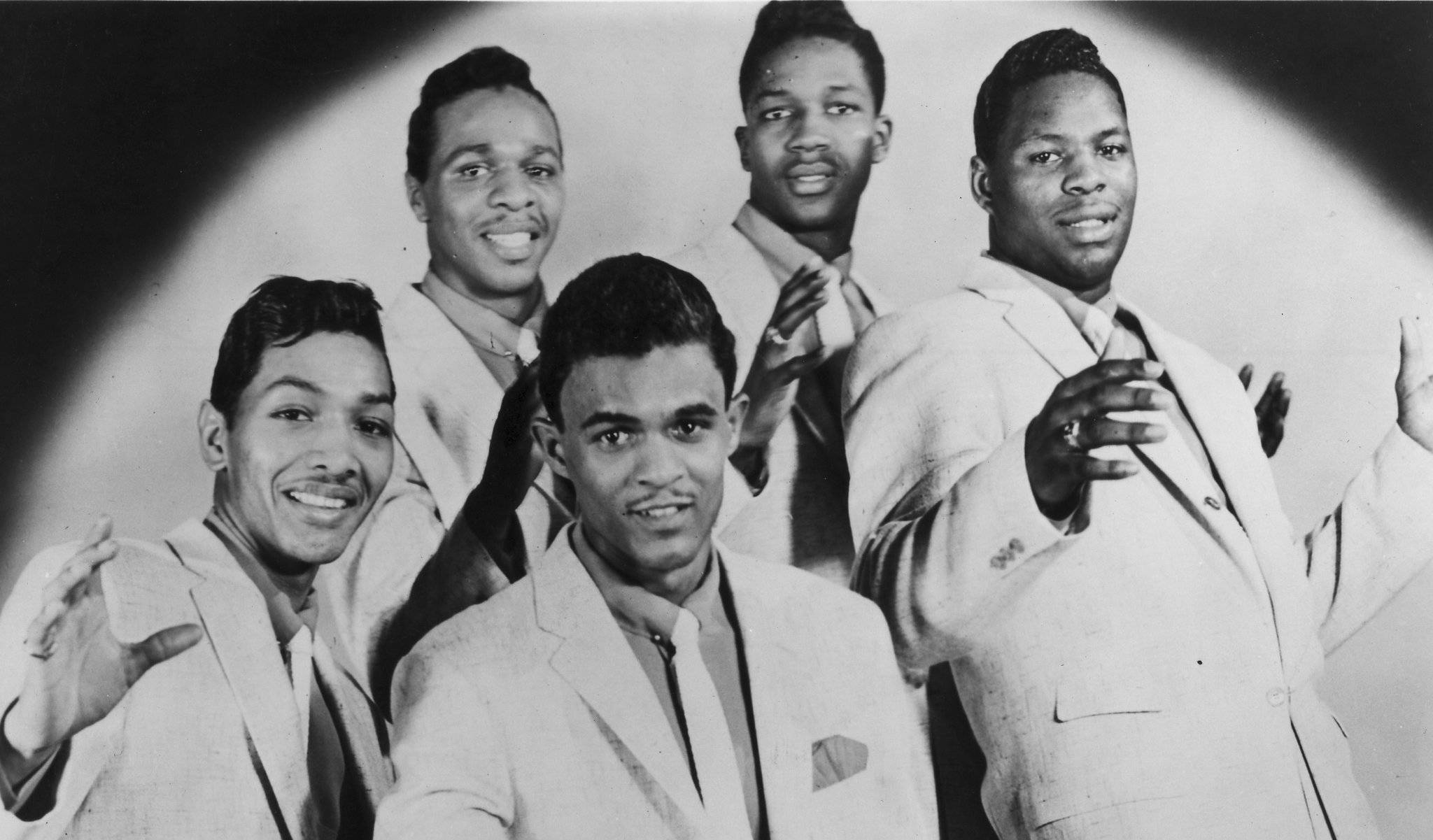 The Dells R&B 壁紙 — 五位微笑的黑人男性穿著淺色西裝，在彎曲的聚光燈背景下自信地擺姿勢，呈現復古工作室肖像。