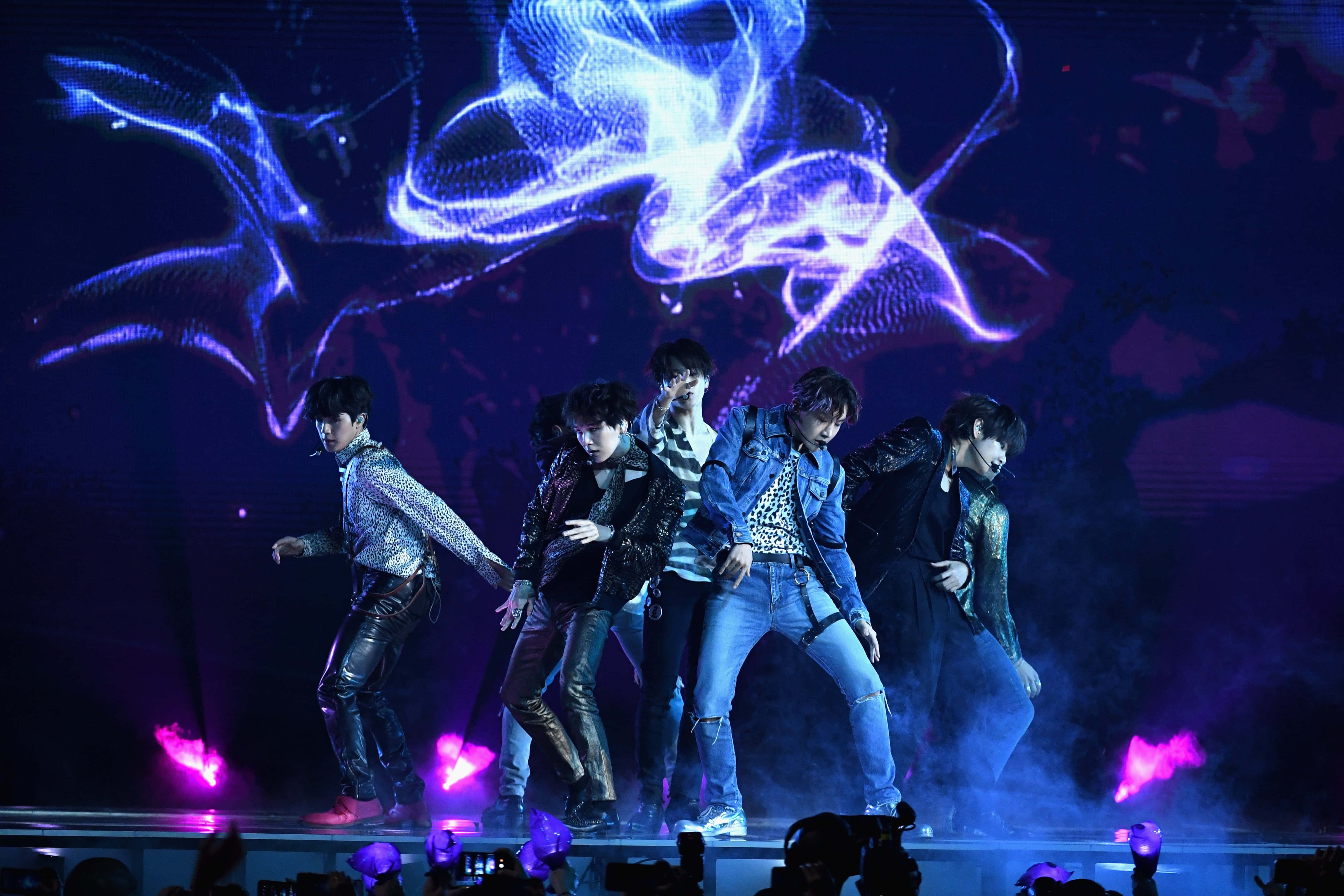 Bts Performance 桌布 壁紙 — 五位男性表演者在閃爍的藍色和紫色舞台燈光下擺出動感舞蹈姿勢，身後有旋轉的數碼投影。