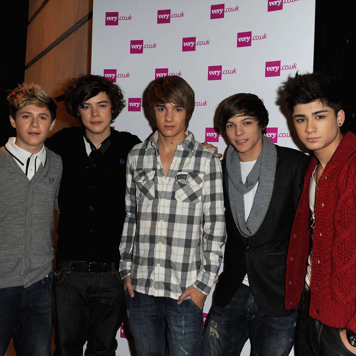 One Direction 桌布 壁紙 — 五位穿著休閒服的年輕男子在活動中一起在品牌背景前擺姿勢。