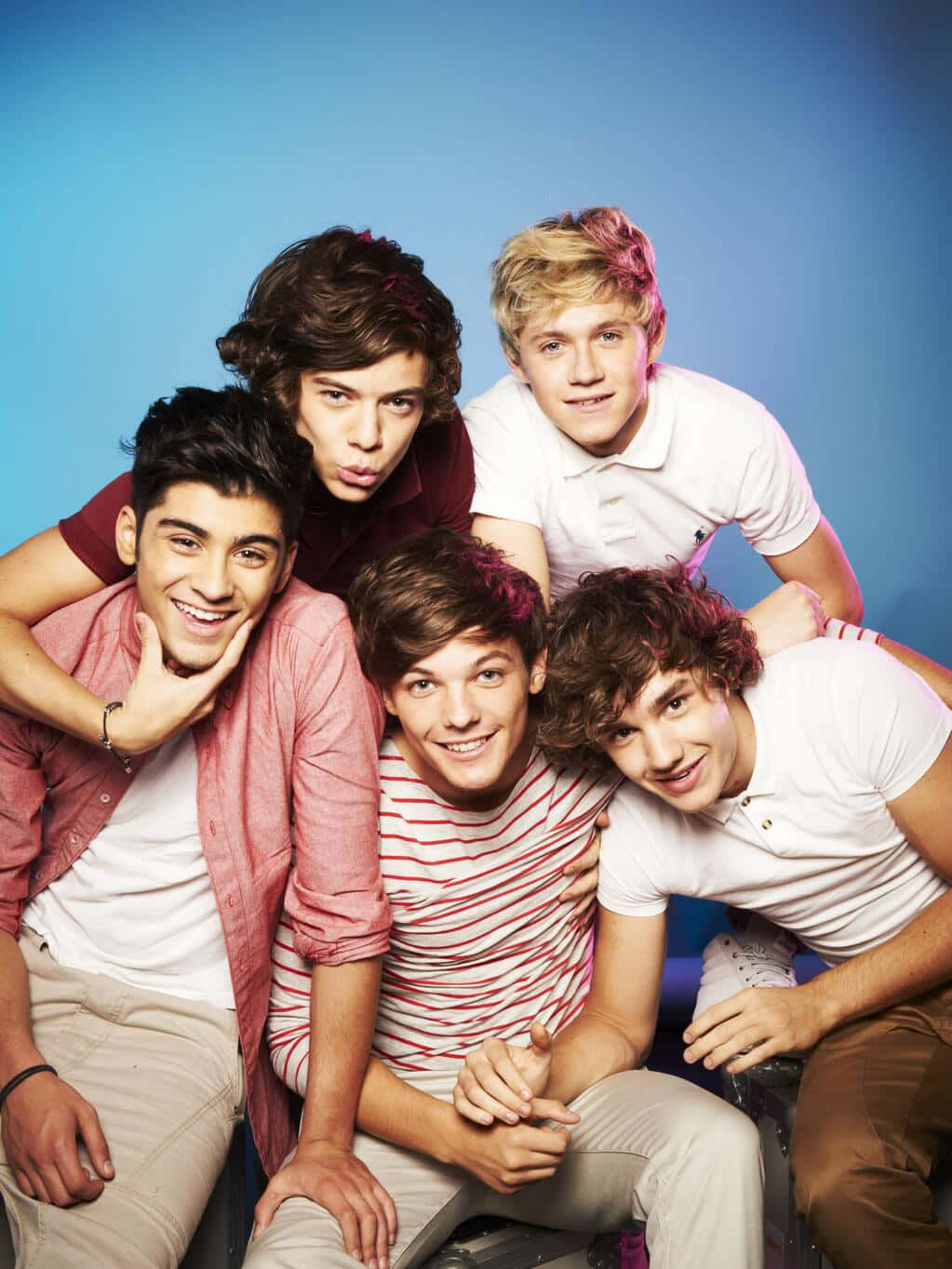 One Direction 桌布 壁紙 — 五位穿著休閒服裝的年輕男性在純藍色攝影棚背景前以多種表情俏皮地擺姿勢。