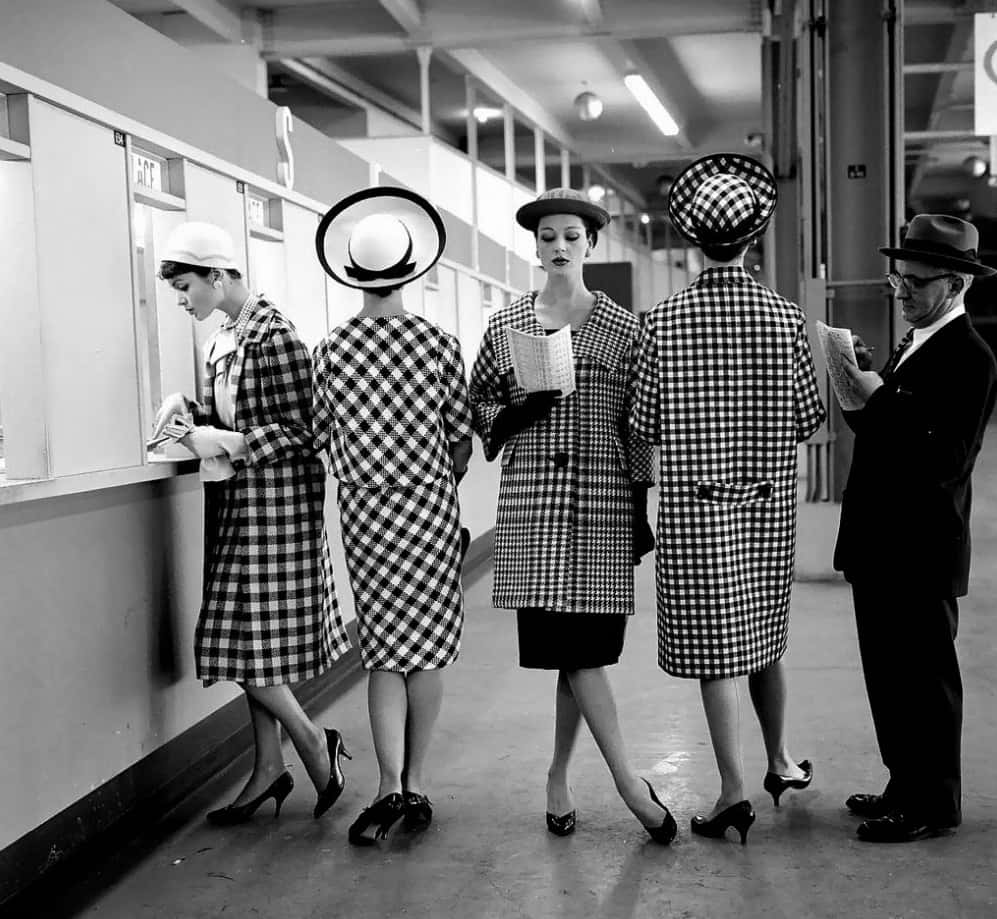 Black And White Fashion 桌布 壁紙 — 五位穿著時尚的1950年代女性，身穿相配的格紋外套和帽子，站在現代主義的走廊裡閱讀報紙。