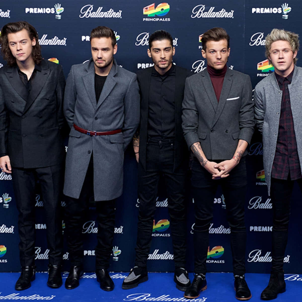 One Direction 桌布 壁紙 — 五位穿著正式服裝的時尚男士在藍色地毯上自信地擺姿勢，背景是品牌活動佈景。