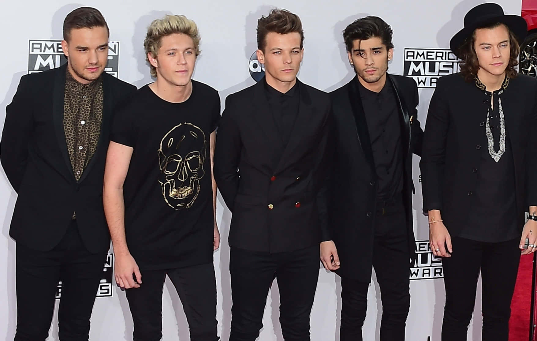 One Direction 桌布 壁紙 — 五位穿著黑色西裝和T恤的時尚年輕男子在頒獎典禮的紅地毯上自信地擺姿勢。