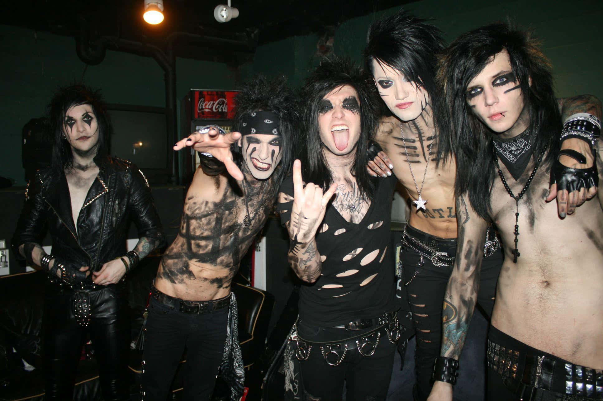 Black Veil Brides 桌布 壁紙 — 五位紋身濃厚的哥德人，化著戲劇性的妝容，在一個光線昏暗、有工業管道和可口可樂標誌的房間裡俏皮地擺姿勢。