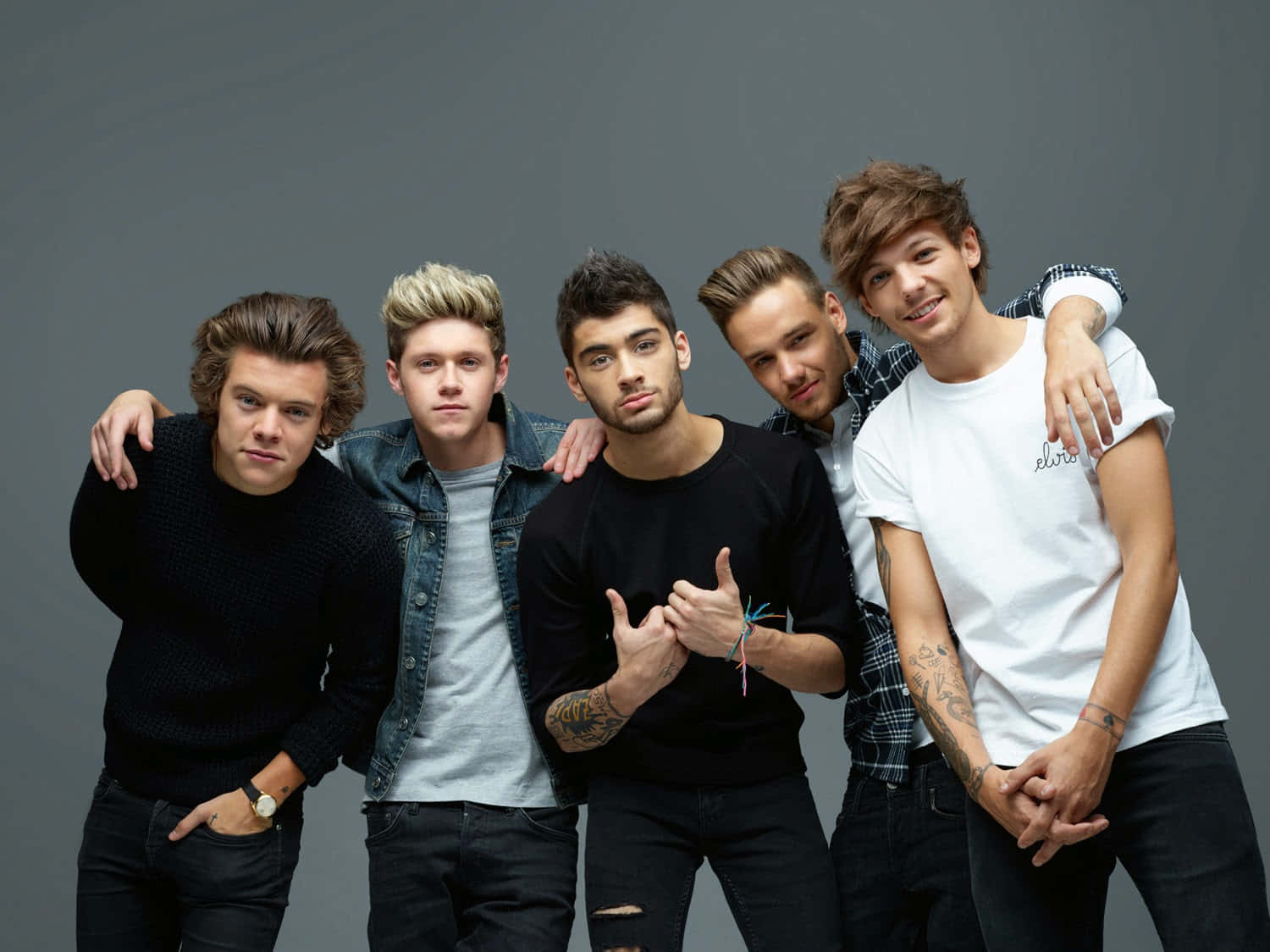 One Direction 桌布 壁紙 — 五位身穿休閒服的年輕男子在純灰色攝影棚背景前自信地擺姿勢，互相搭著肩膀。