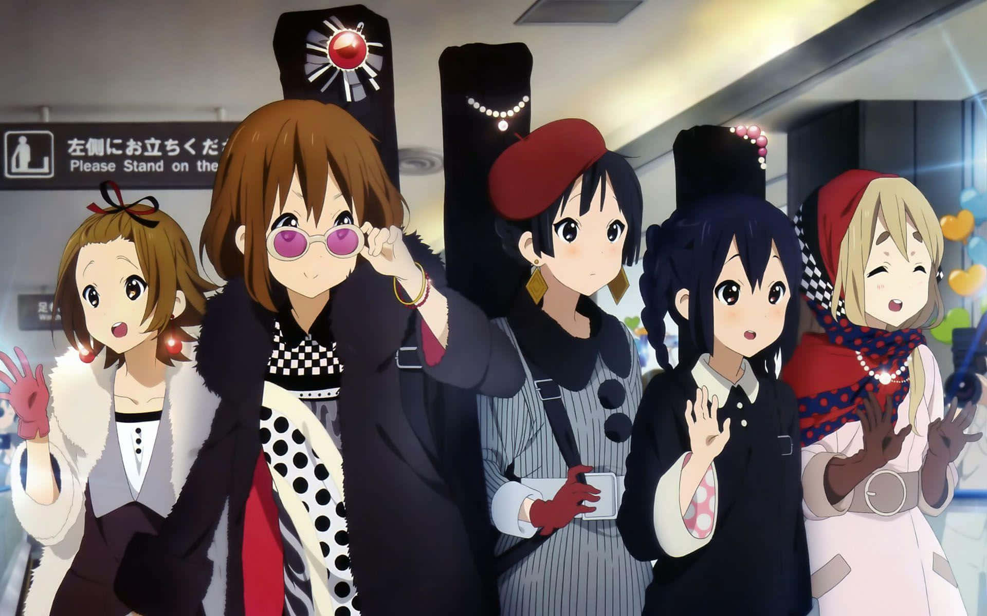 K-on 桌布 壁紙 — 五位身穿時尚服裝的動漫女孩在光線明亮的室內車站（帶有日語標牌）中愉快地揮手。