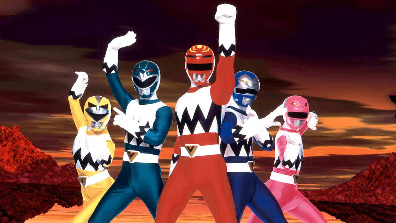 Power Rangers 桌布 壁紙 — 五位身穿色彩繽紛戰衣的Power Rangers在紅色岩石地形上，以英雄姿態對抗熾熱的夕陽。