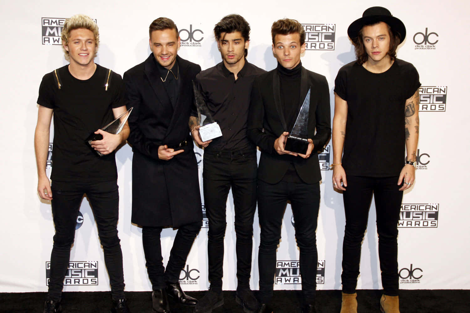 One Direction 桌布 壁紙 — 五位身穿黑色服裝的年輕男性在美國音樂獎的白色品牌背景前手持獎項擺姿勢。