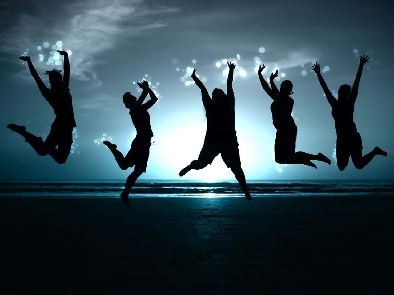 Youthful 桌布 壁紙 — 五個剪影人物在黃昏的海灘上歡樂跳躍，身後天空中有發光的散景燈光。