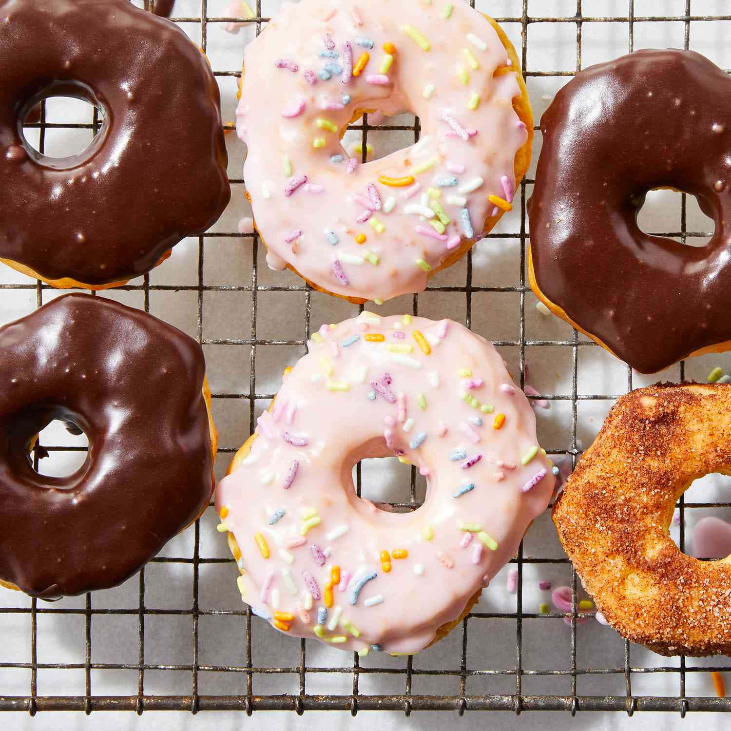 Glazed Donut 桌布 壁紙 — 五個塗有朱古力和粉紅色糖霜、頂部撒上彩色糖粒的釉面冬甩放在金屬冷卻架上。