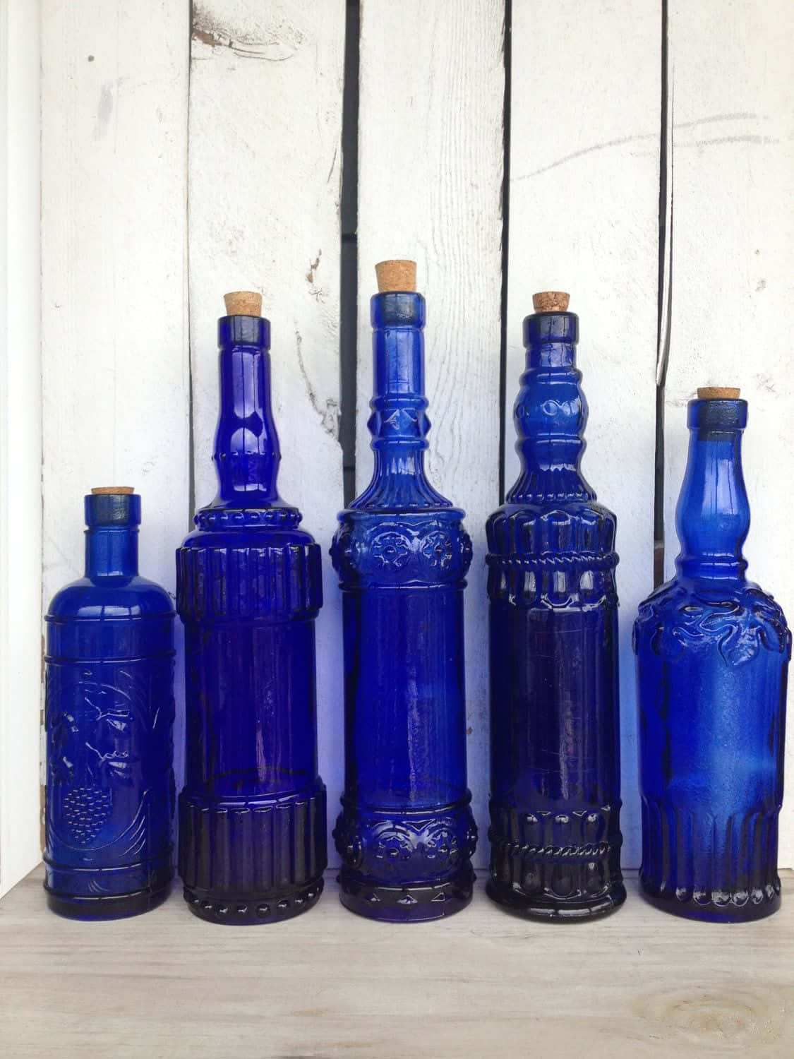 Cobalt Blue 桌布 壁紙 — 五個帶軟木塞的鈷藍色復古玻璃瓶排成一排，背景是風化的白色木板。