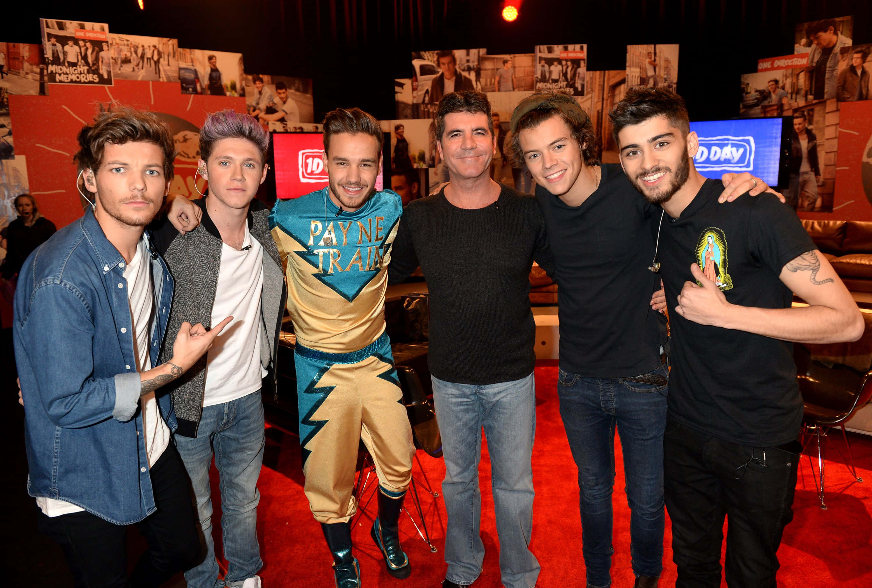 One Direction 桌布 壁紙 — 五個男人一起在紅地毯上擺姿勢，其中一人穿著色彩繽紛的Payne Train服裝，周圍環繞著照片和電視屏幕。