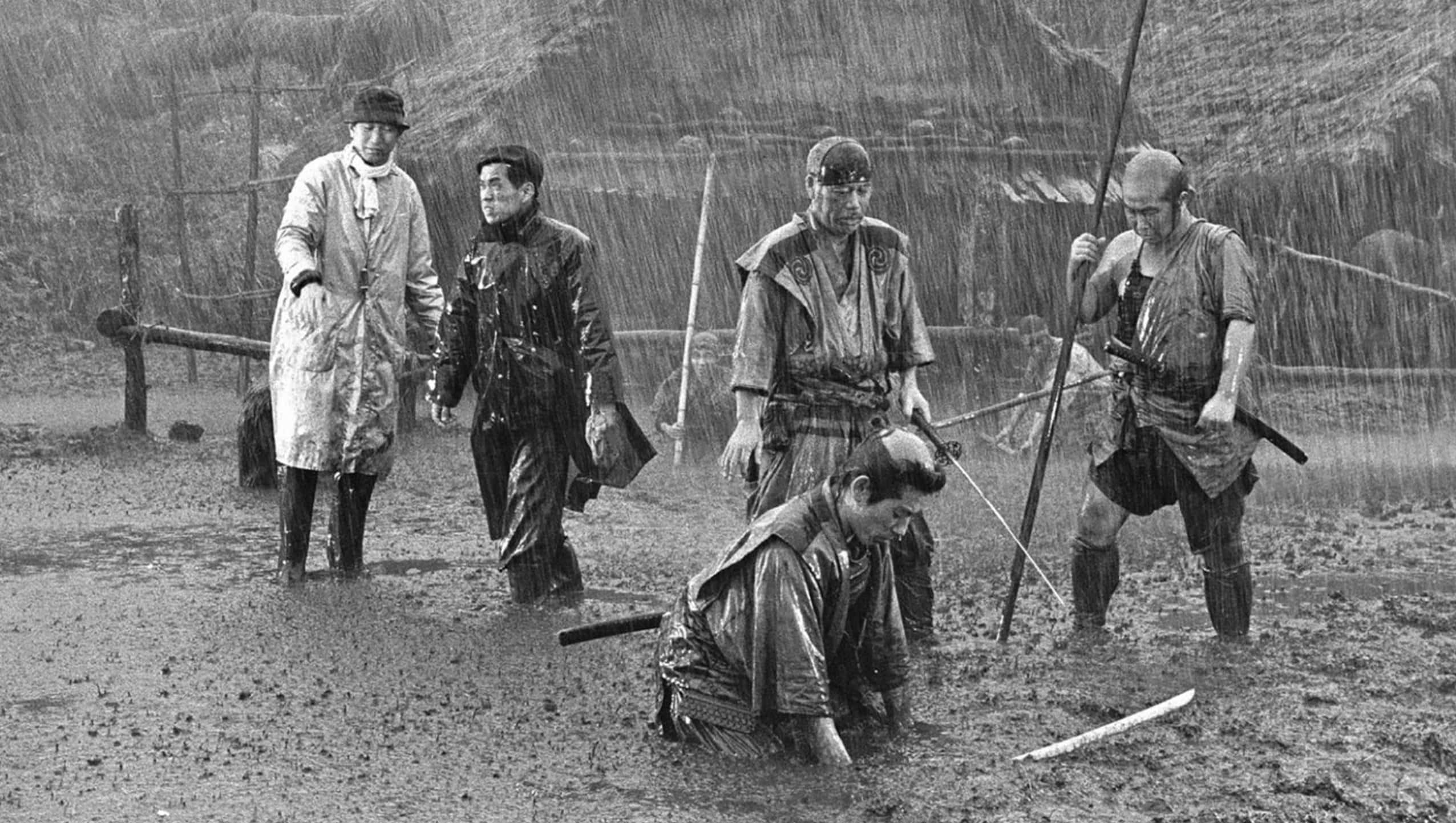 Akira Kurosawa 桌布 壁紙 — 五個身穿傳統服飾、被雨淋濕的男人在泥濘的地形上，在暴雨中站立和跪著，附近有劍。