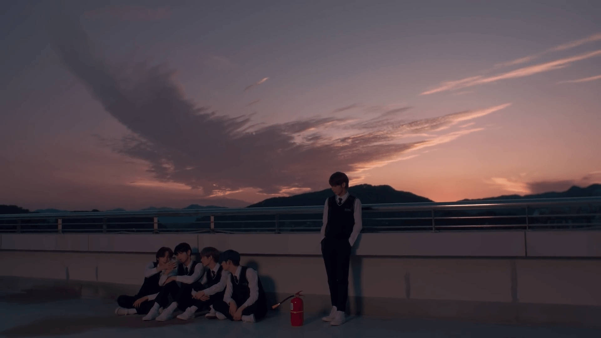 Tomorrow X Together Run Away 壁紙 — 五名年輕男子身穿相配的黑色背心，在黃昏時分坐在或站在屋頂上，背後是山脈和粉紫色的天空。