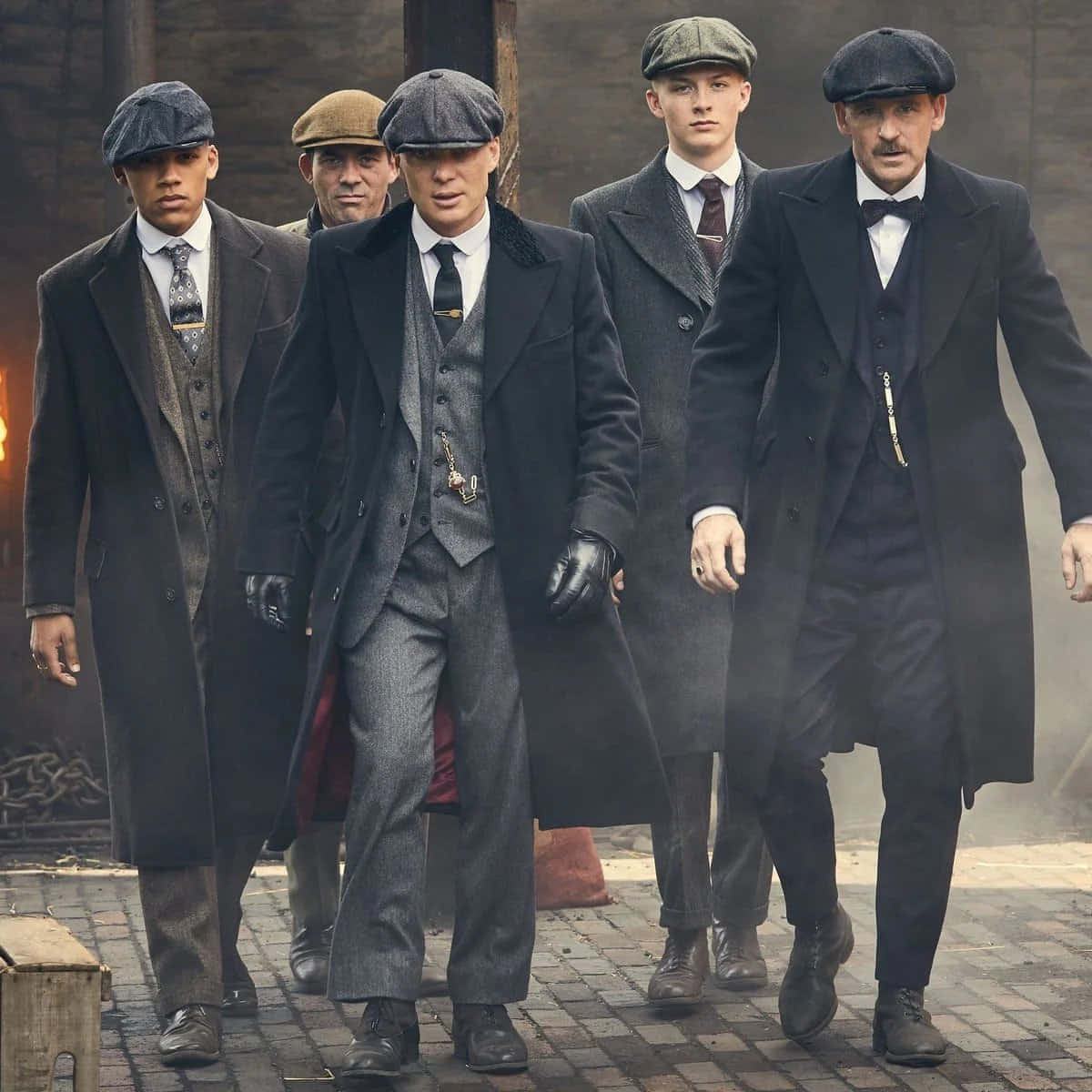 Peaky Blinders 桌布 壁紙 — 五名戴著復古平頂帽、身穿大衣的男子，在霧氣瀰漫的磚街上自信地大步前行，背景是粗獷的城市環境。