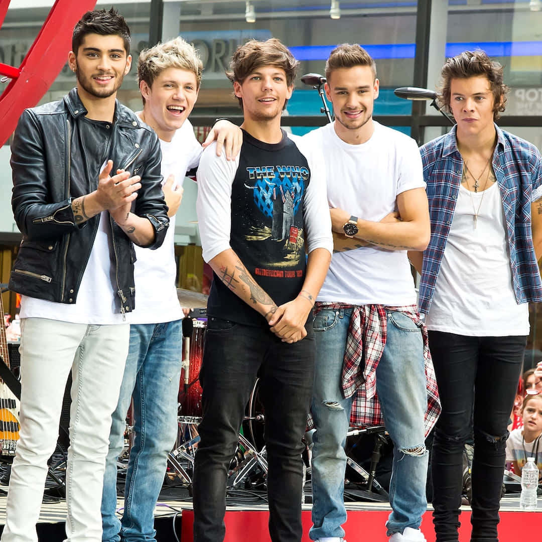 One Direction 桌布 壁紙 — 五名身穿休閒街頭服的年輕男子在紅色舞台上一起擺姿勢，身後有樂器。