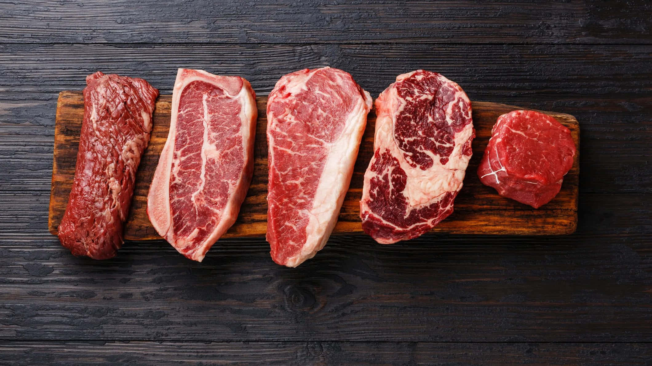 meat 桌布 壁紙 — 五塊帶有大理石紋的未經烹調牛肉，排列在木板上，背景為深色鄉村風格木材。