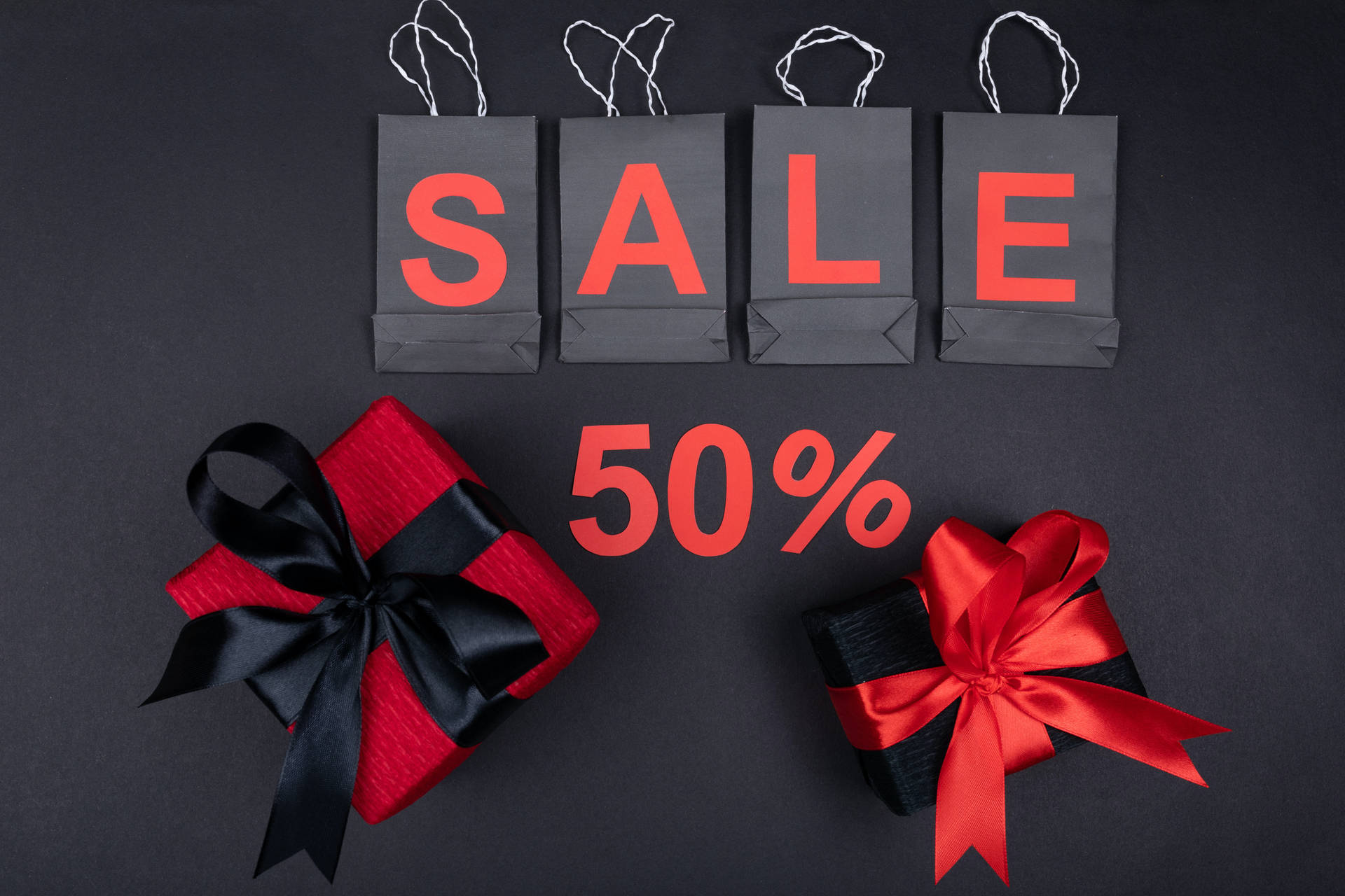 黑色購物袋拼出SALE，附有50%折扣文字，以及兩個附有紅色和黑色蝴蝶結的包裝禮物。