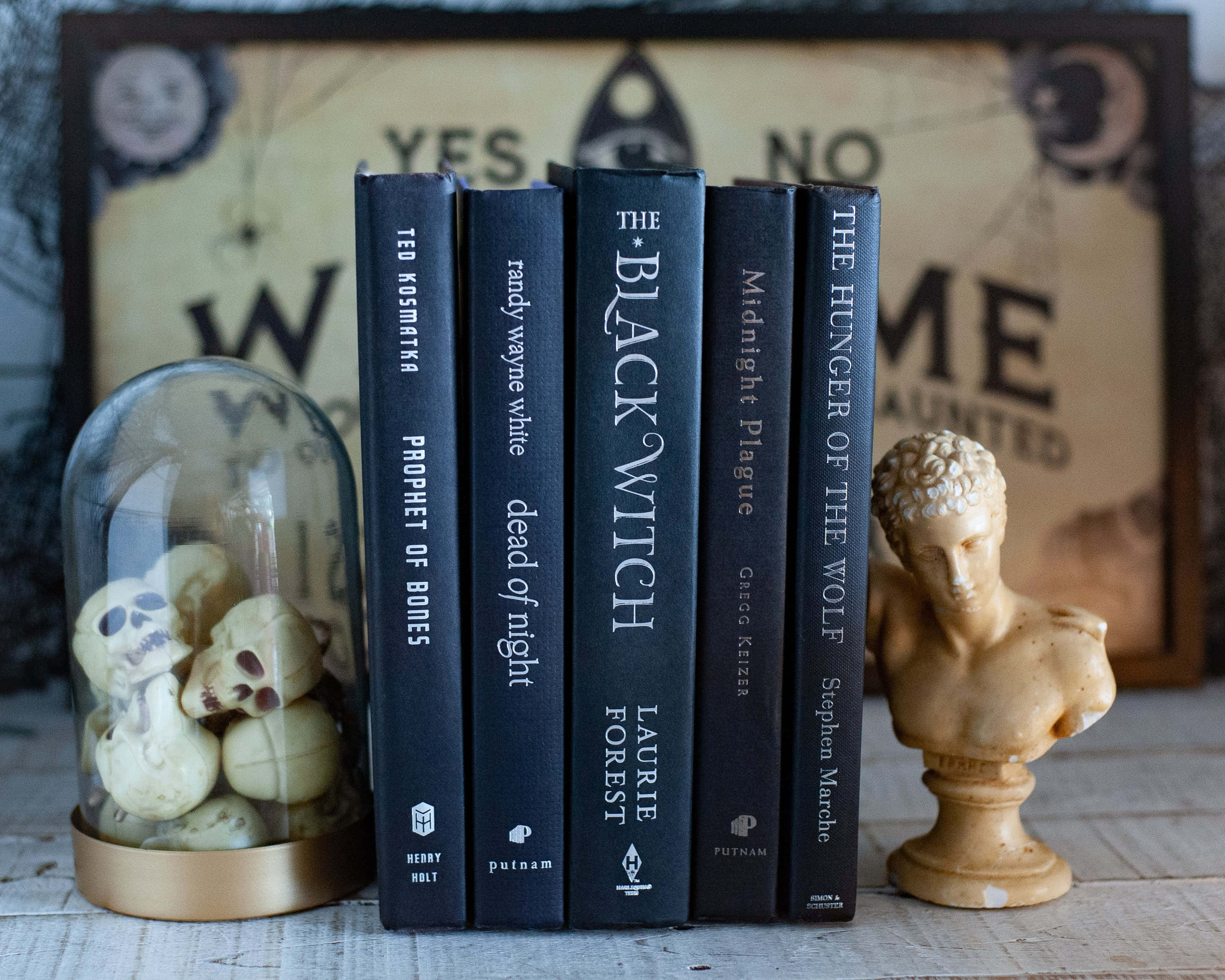 Halloween Books 桌布 壁紙 — 五本黑暗奇幻書籍矗立在一個帶有頭骨的玻璃穹頂和一個石像半身像之間，背景是神秘的有框背景。