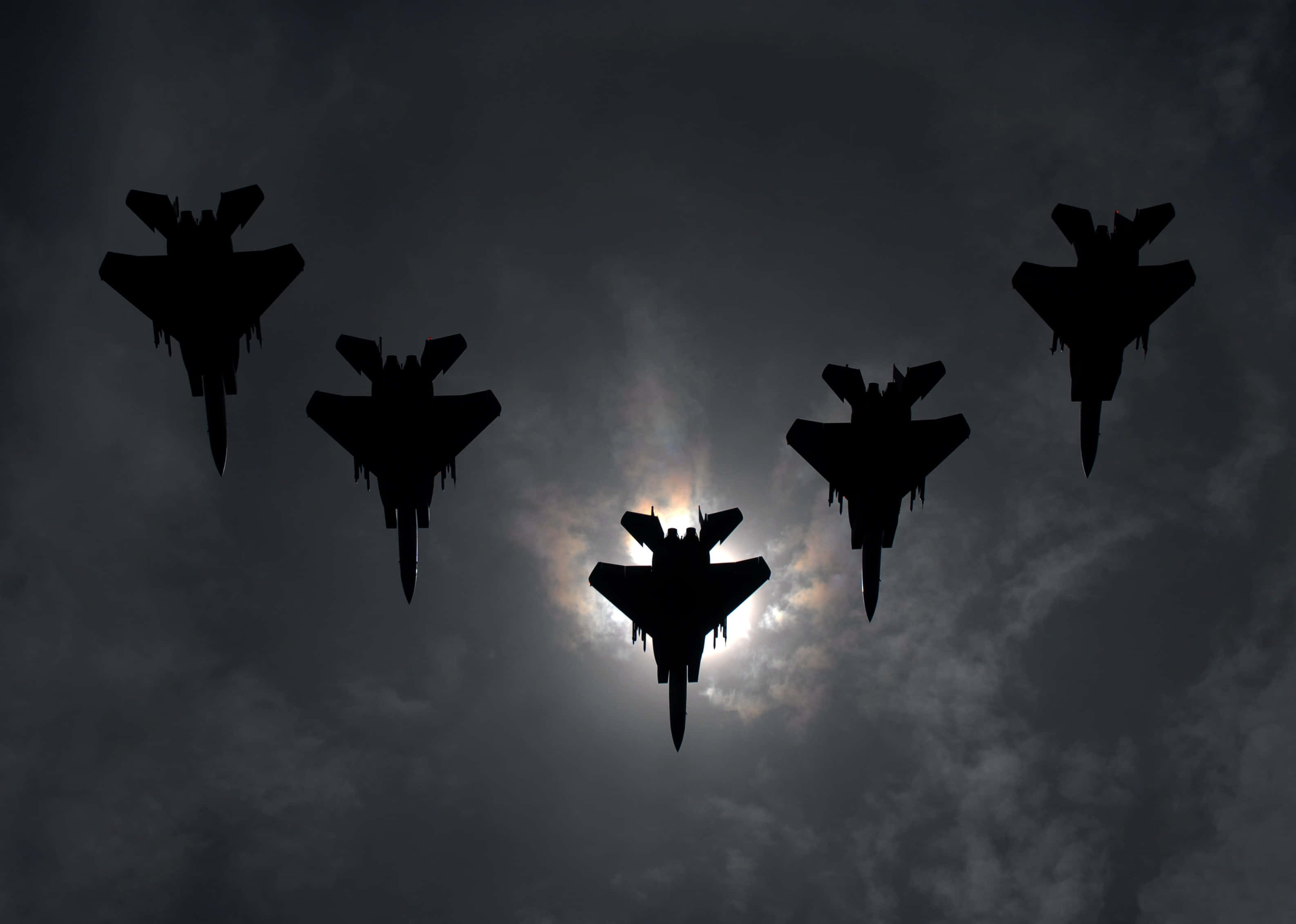 Air Force 桌布 壁紙 — 五架戰鬥機在陰暗多雲的天空中以緊密編隊飛行，太陽在它們背後發光。