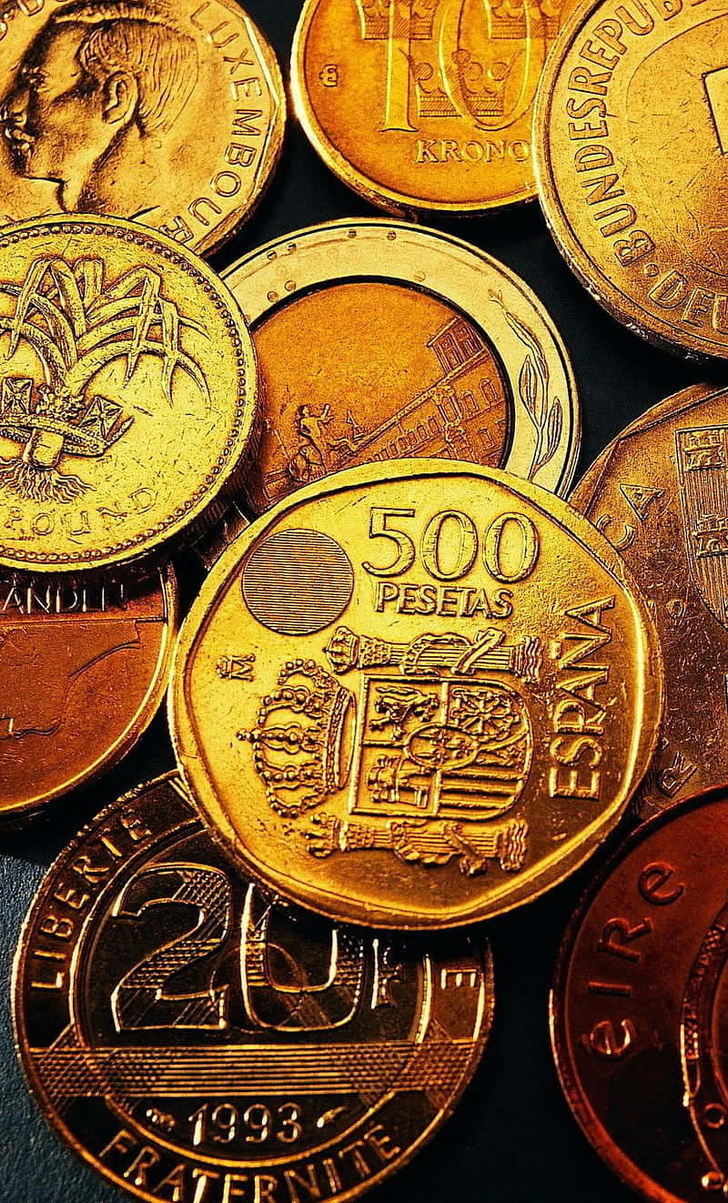 五百比塞塔金幣 壁紙 — 不同國家的金色和銅色硬幣散落在深色表面上的特寫。