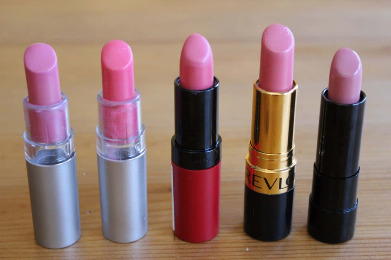 Pink Lipstick 桌布 壁紙 — 五種不同粉紅色調的唇膏直立展示在淺色木質表面上。