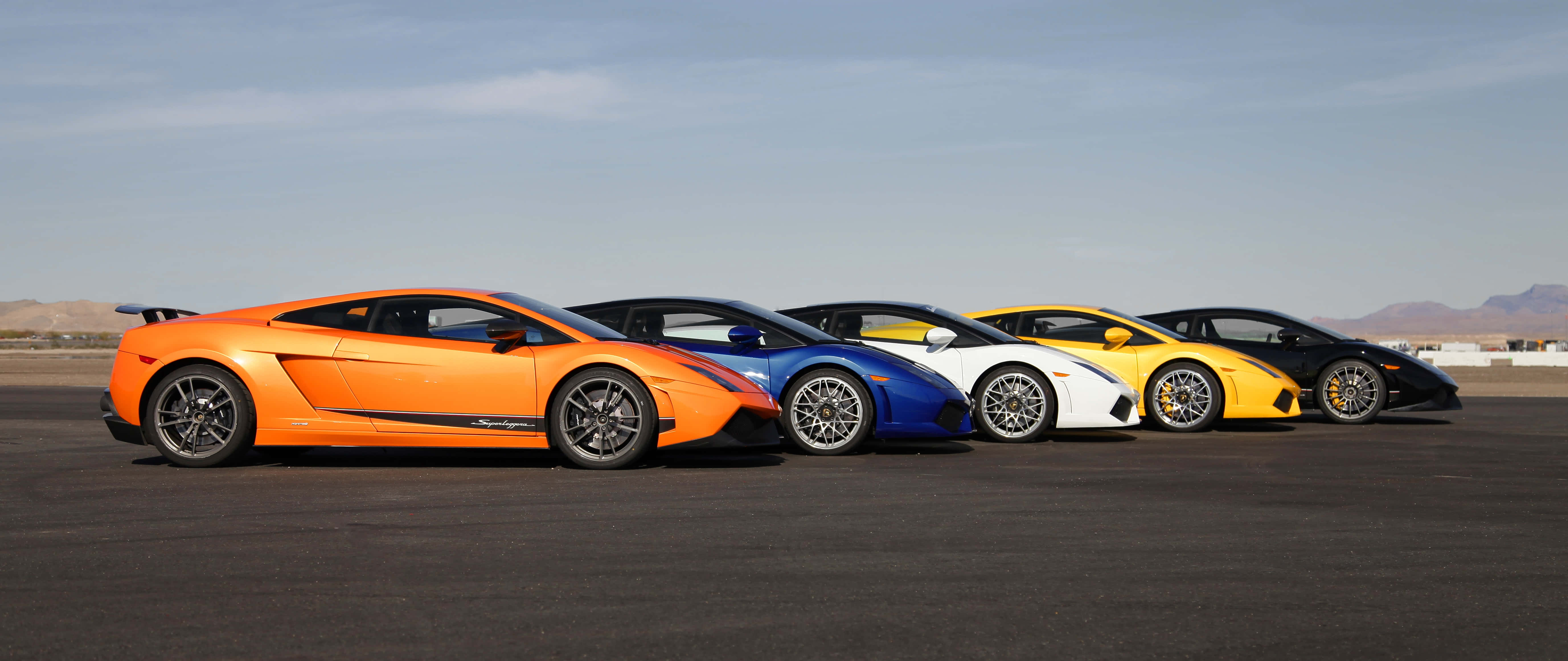 Car Racing 桌布 壁紙 — 五輛色彩鮮豔的林寶堅尼Gallardo，橙色、藍色、白色、黃色和黑色，在晴朗的天空下排列在沙漠賽道上。