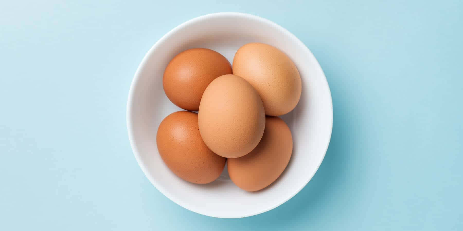 Egg 桌布 壁紙 — 五隻棕色雞蛋放在一個白色碗裡，襯著柔和的藍色背景。