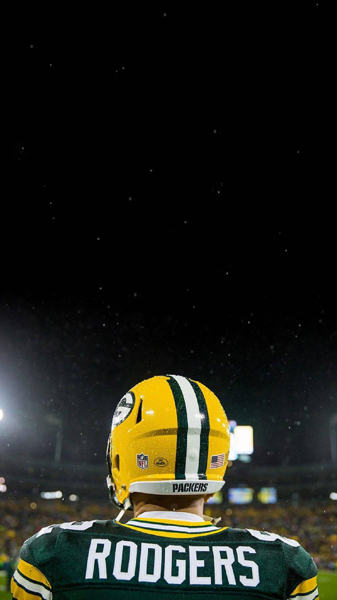 亞倫·羅傑斯 NFL比賽之夜 壁紙 — 在雪夜球場的體育場燈光下，從背後看到的綠灣包裝工美式足球員。