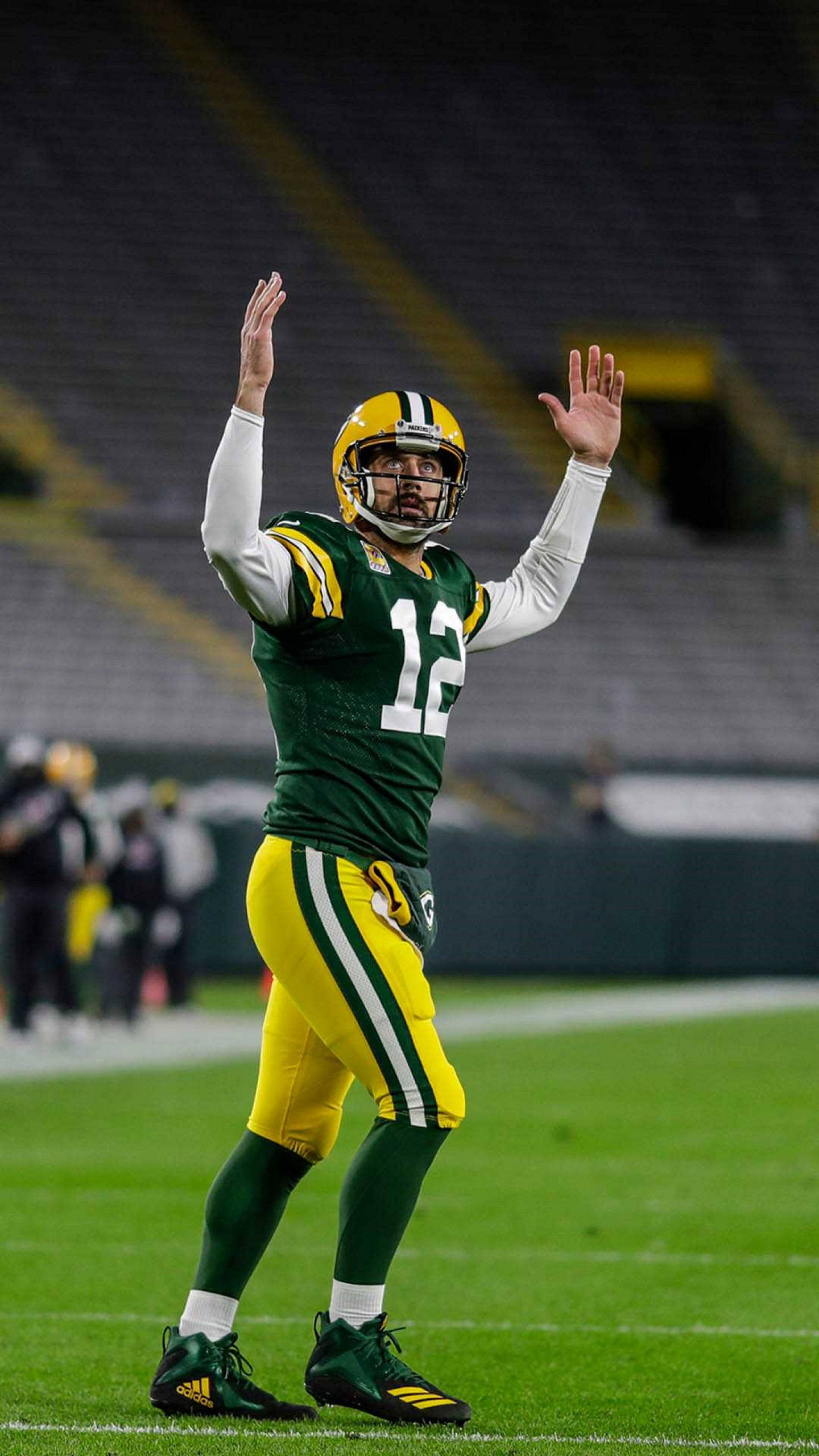 亞倫·羅傑斯 綠灣NFL 壁紙 — 一位身穿綠黃色球衣的綠灣包裝工四分衛在明亮燈光下的球場上向球迷揮手。