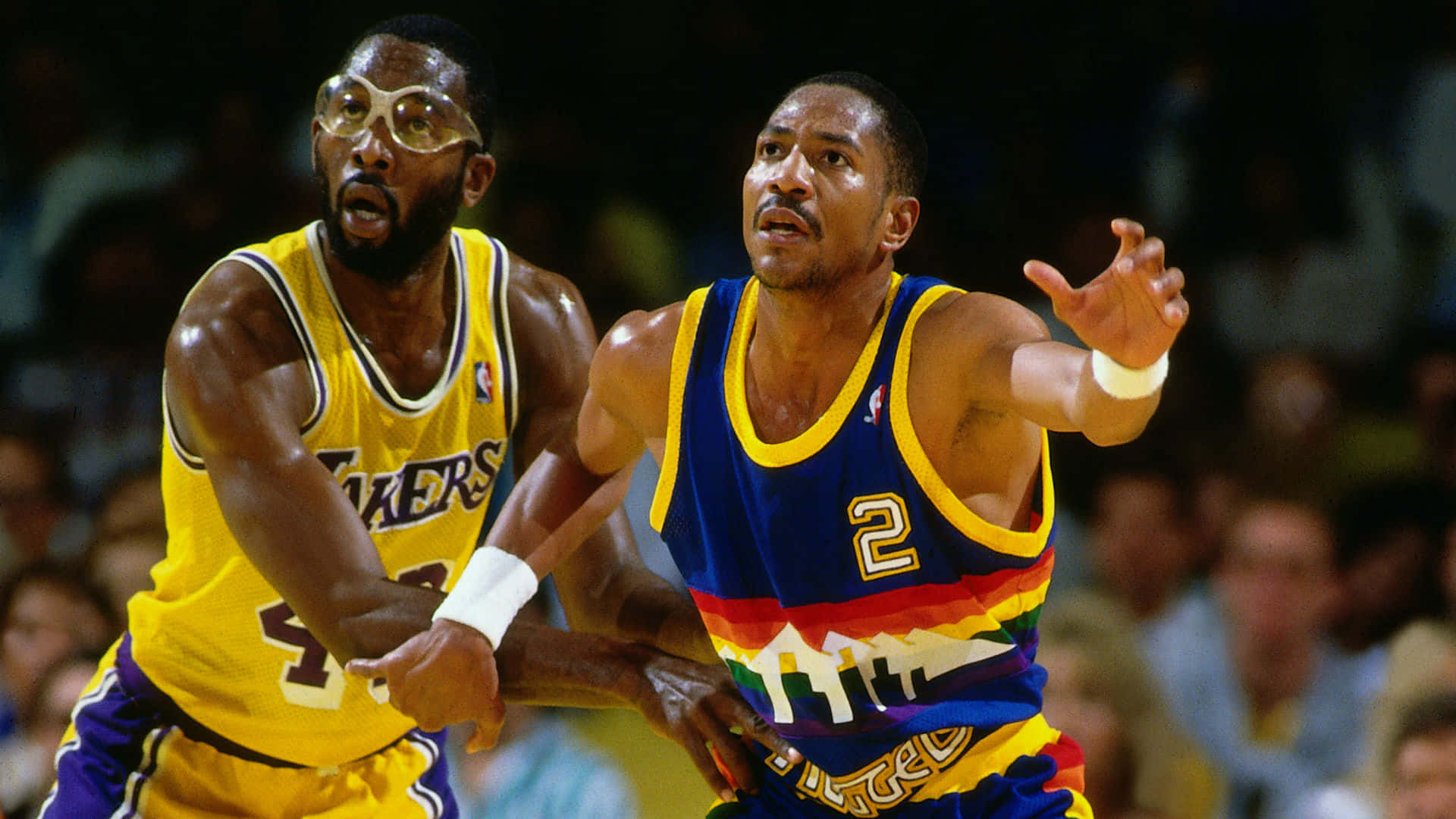 兩名NBA籃球運動員在比賽中行動，一人身穿湖人隊球衣，另一人身穿丹佛金塊隊球衣。