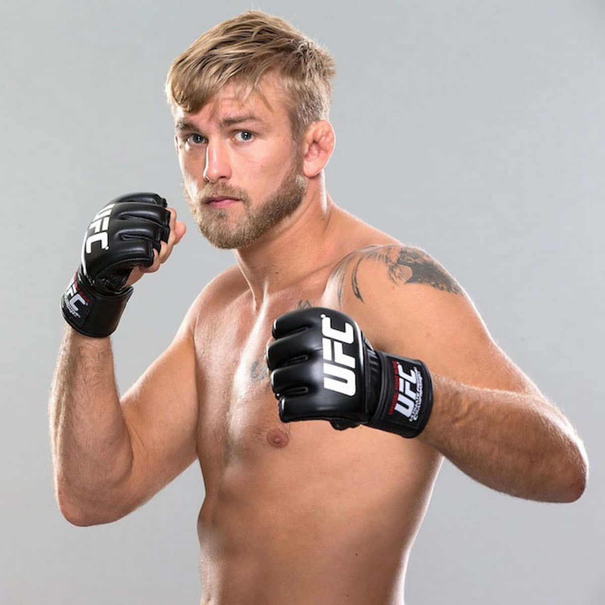 一位赤裸上身的男性綜合格鬥選手戴著黑色UFC手套，擺出專注的表情。