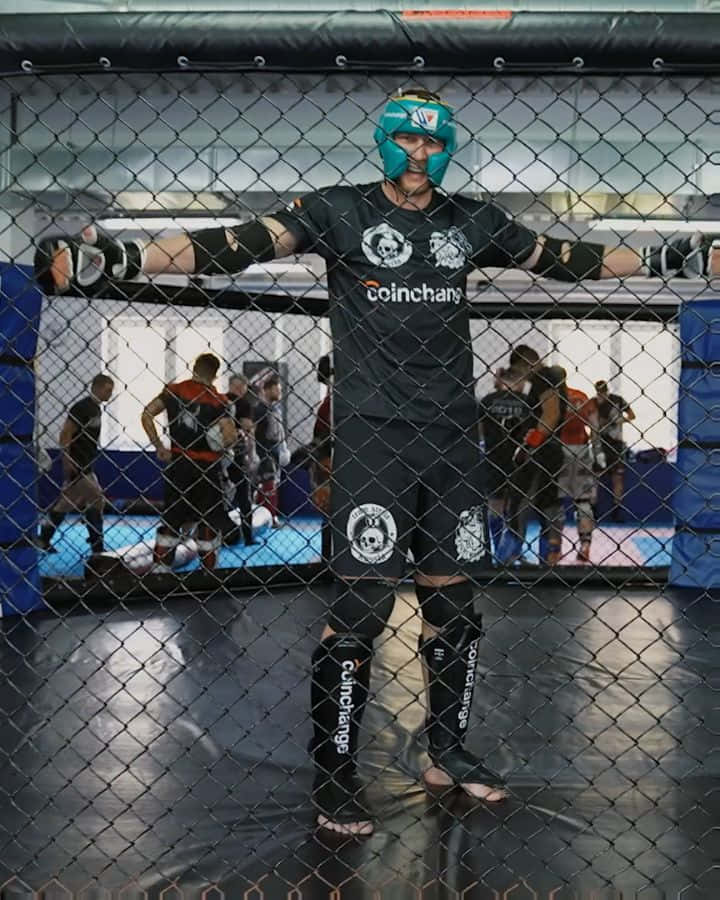 身穿裝備的MMA戰士站在鐵籠內，其他人在訓練。